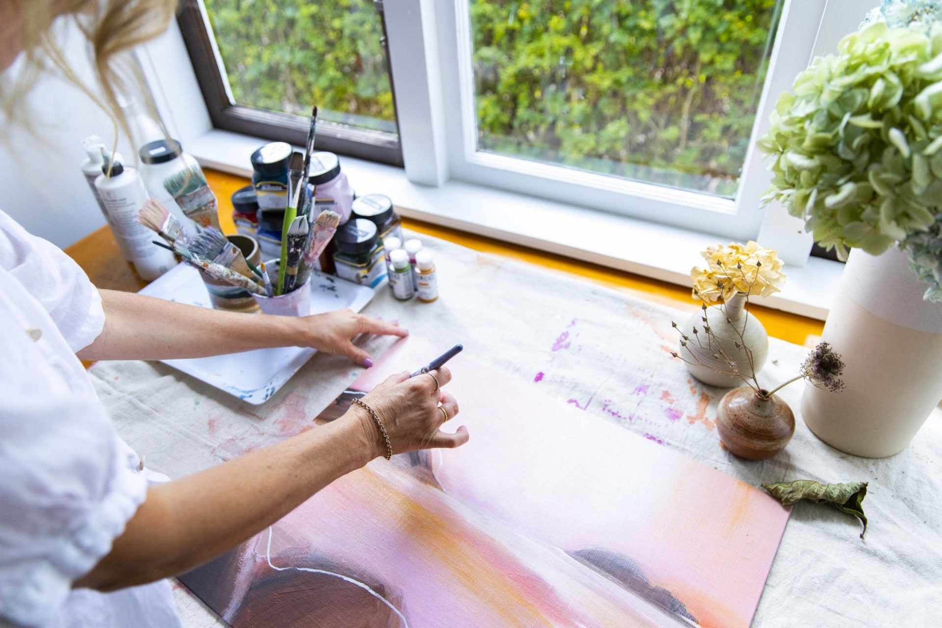 Over the shoulder of Brenda Clews painting pink and orange sunset 