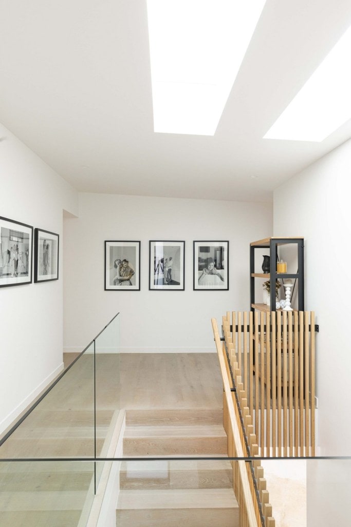 Bright white hallway with light timber floor and wooden stair handrail and black and white photos on the wall