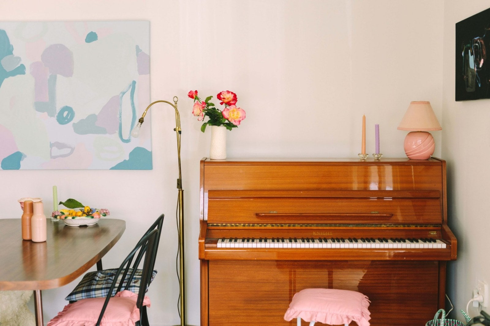 Hnědé piano s pastelovou židlí, růžovou lampou a vázou s květinami