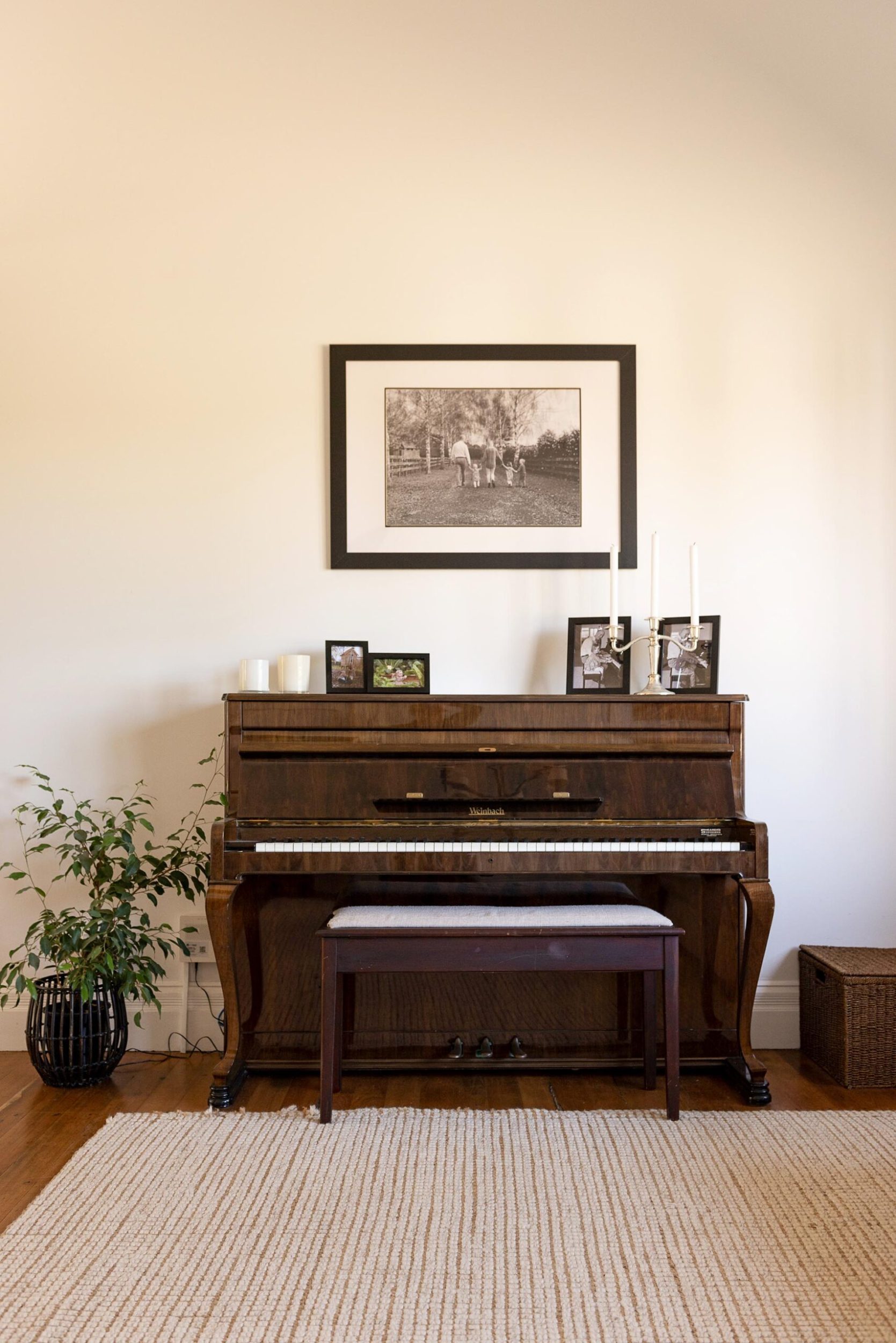 A dark wood piano with black and white portraits on top in a white room