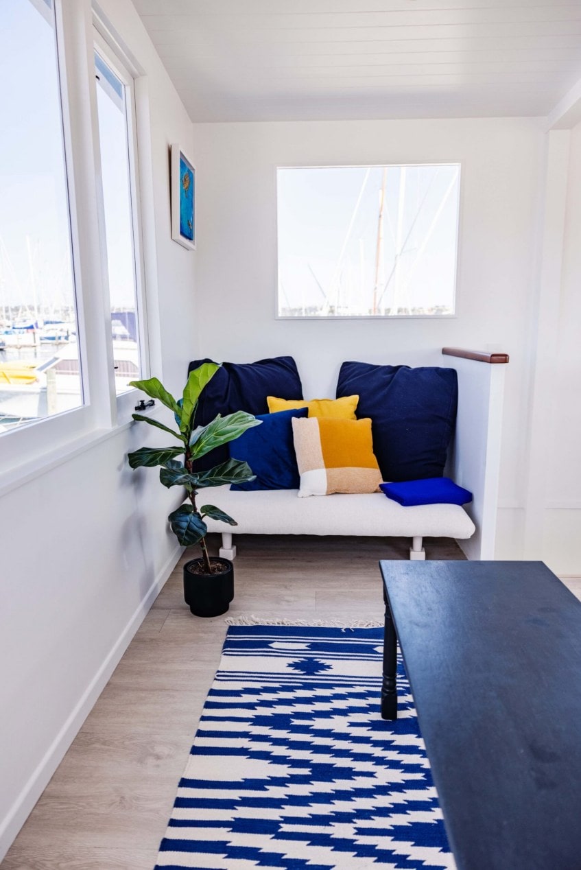 Sitting space within a houseboat with a white couch and blue pillows and patterned rug