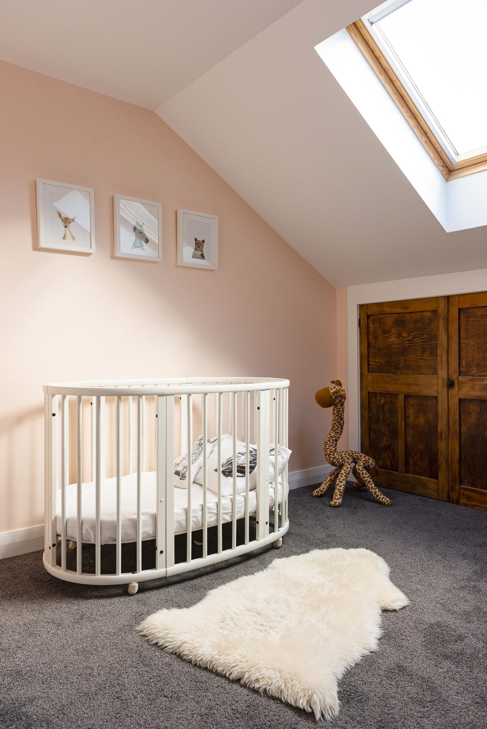A baby room with pink walls, arched ceiling with a ceiling light and a round white cot