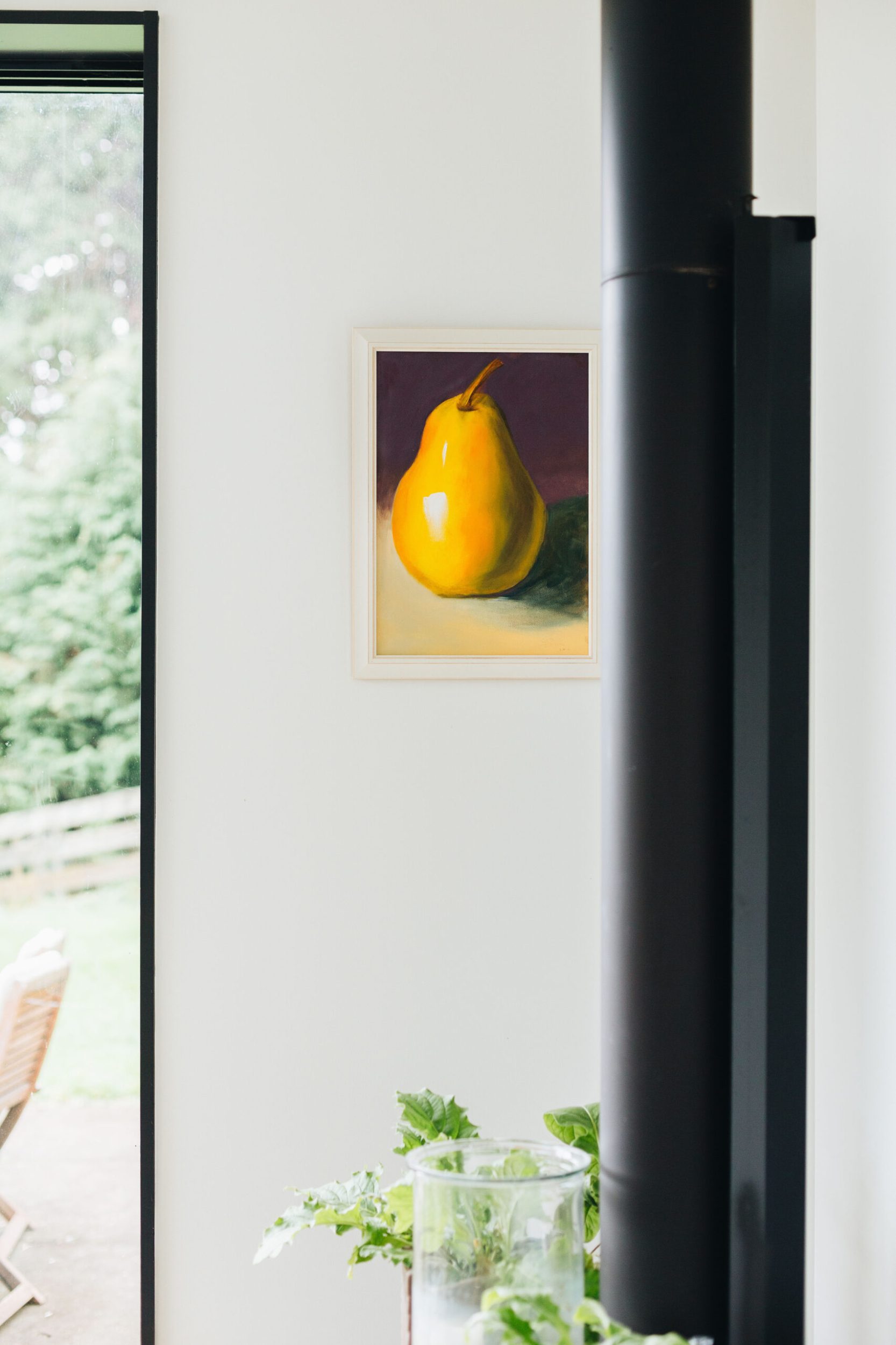 A painting of a yellow pear hanging on a white wall next to a black fireplace chute