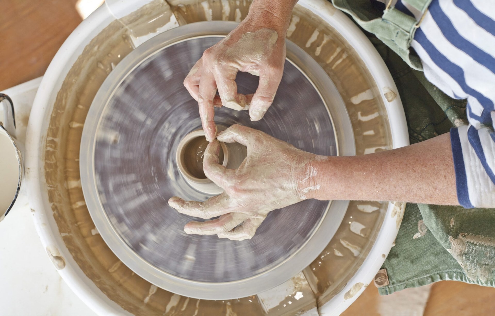 Woman's hands creating a round vase on a pottery wheel