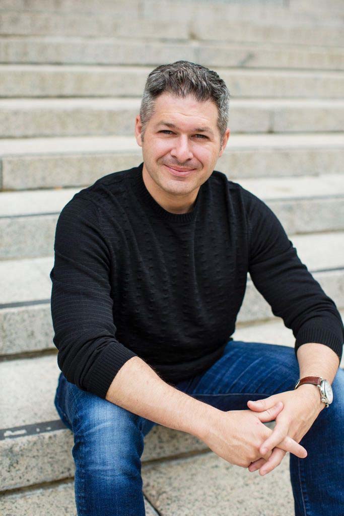 Headshot of Professor Ethan Kross sitting on grey steps