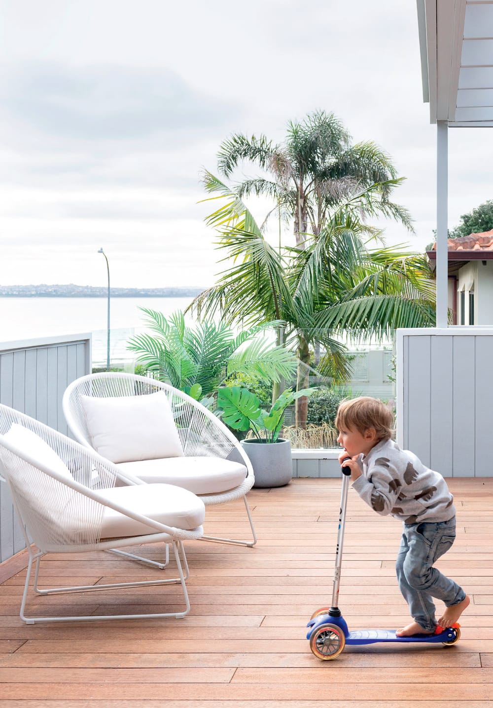 Young boy rides a scooter on a deck with two white chairs