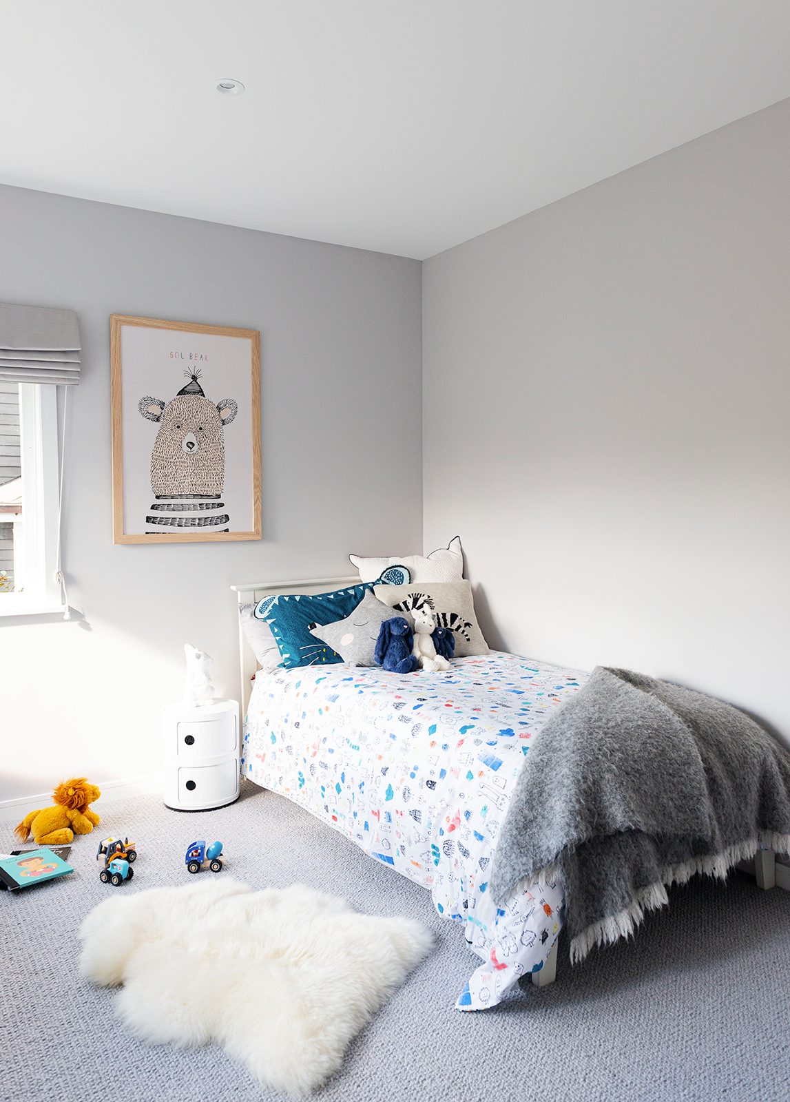 Kinds bedroom with colourful bedlinen, sheepskin on the floor and illustration of bear on the walls