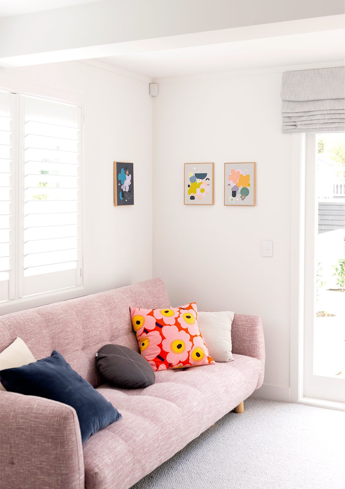 Pink couch with colourful cushions and artwork on the walls
