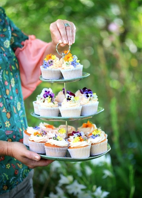 A woman's hand holding a plate of cupcakes with icing covered in petals