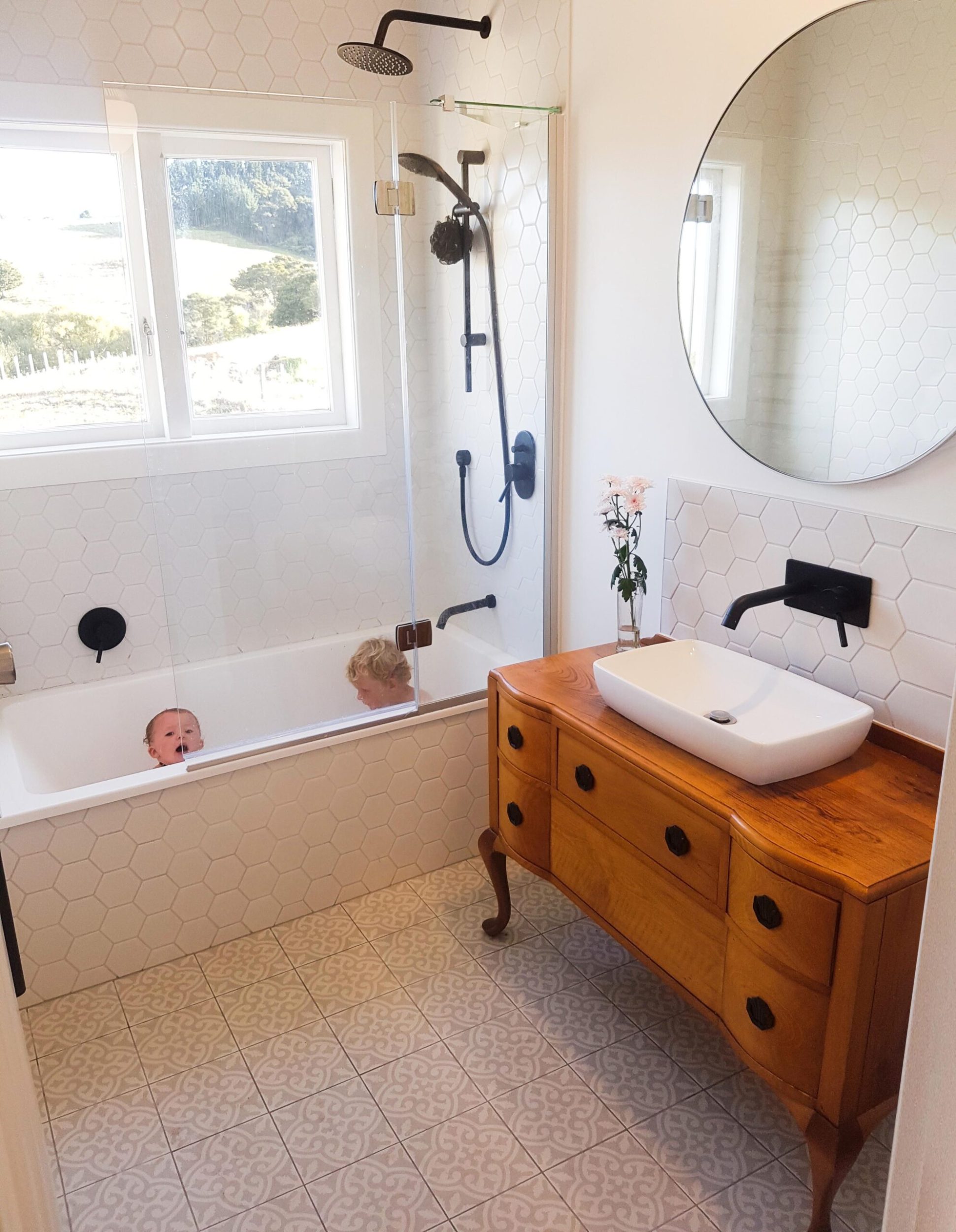 A bathroom with a large round mirror and sink vanity made out of a upcycled wood dresser