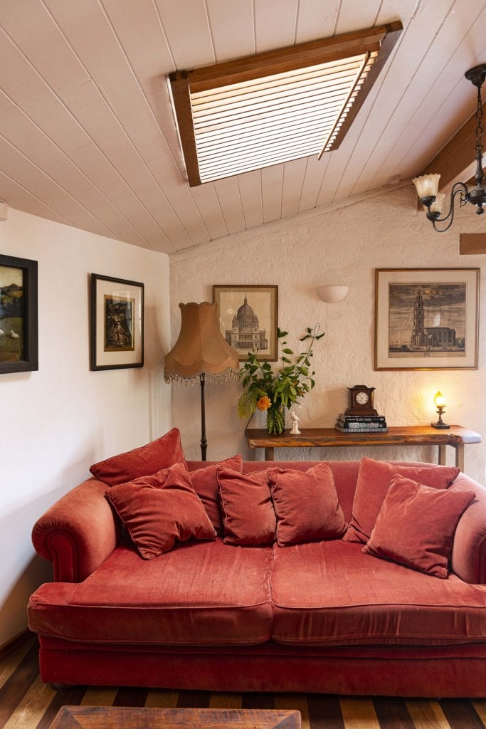 A living room with white walls, vintage black and white hanging art, a plush red couch and an angled ceiling