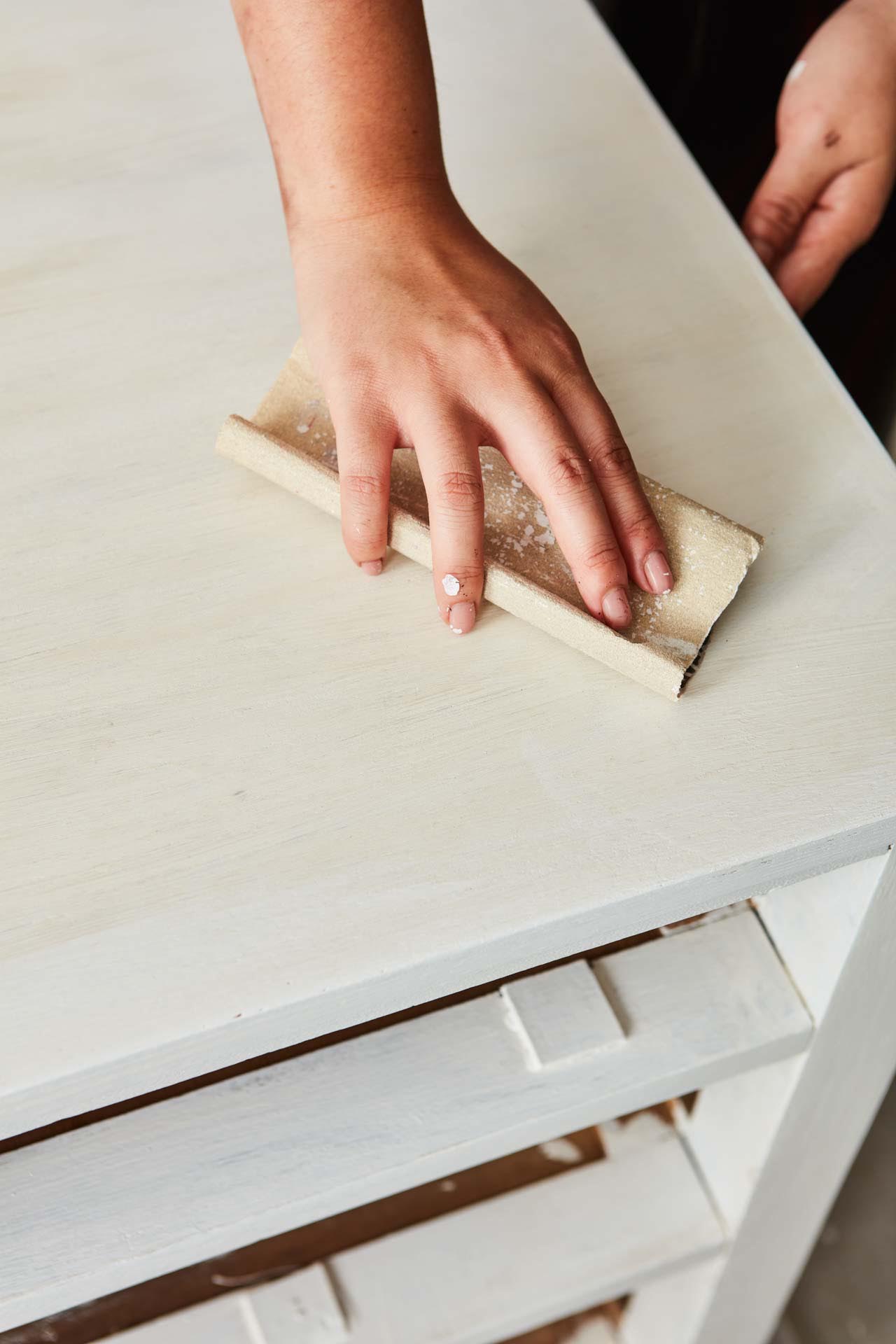 Hands sanding a painted chest of drawers