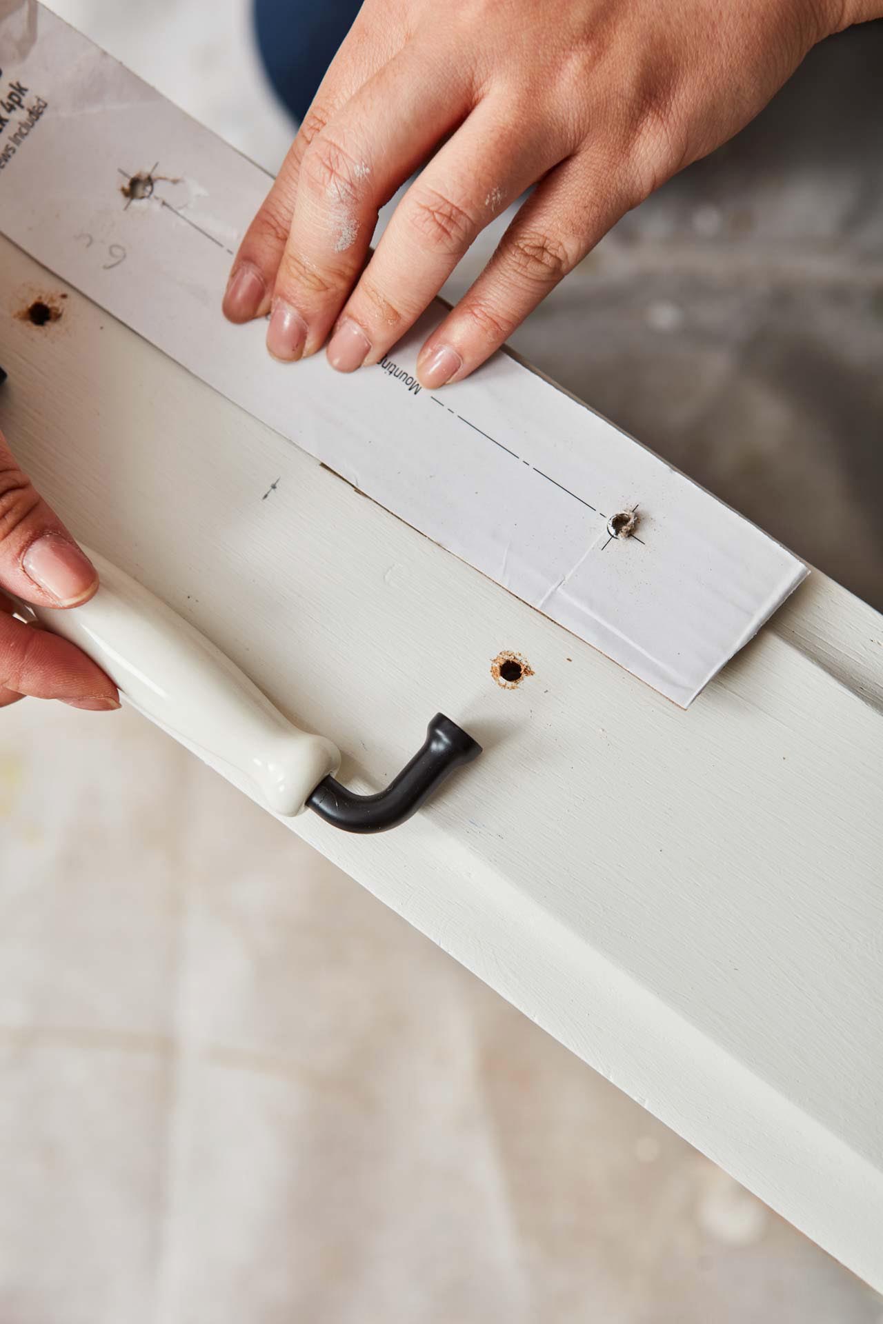 Using cardboard template to measure holes for new handles in chest of drawers