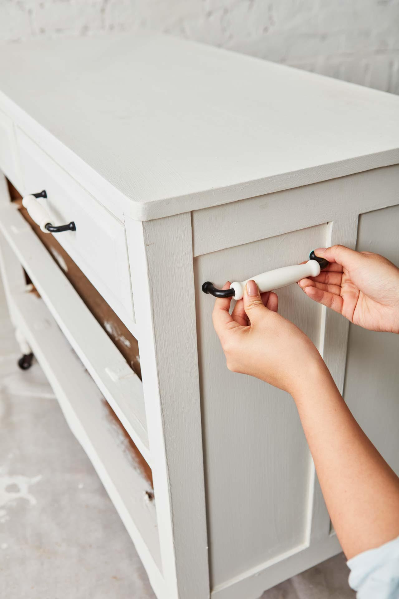 Hands holding new handle up to painted chest of drawers