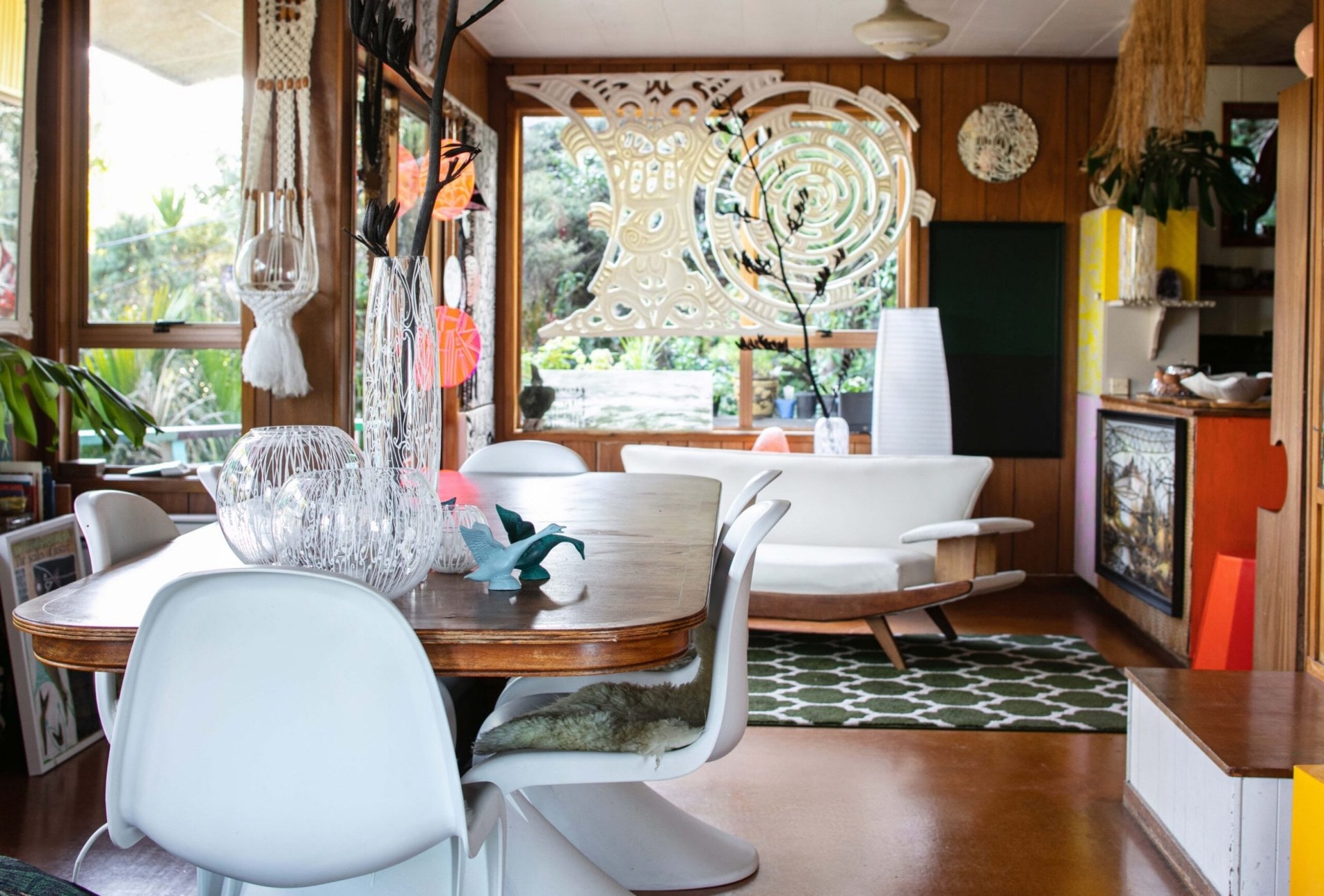 A living room with wood panels with assorted hanging Māori styled art by Tracey Tawhiao