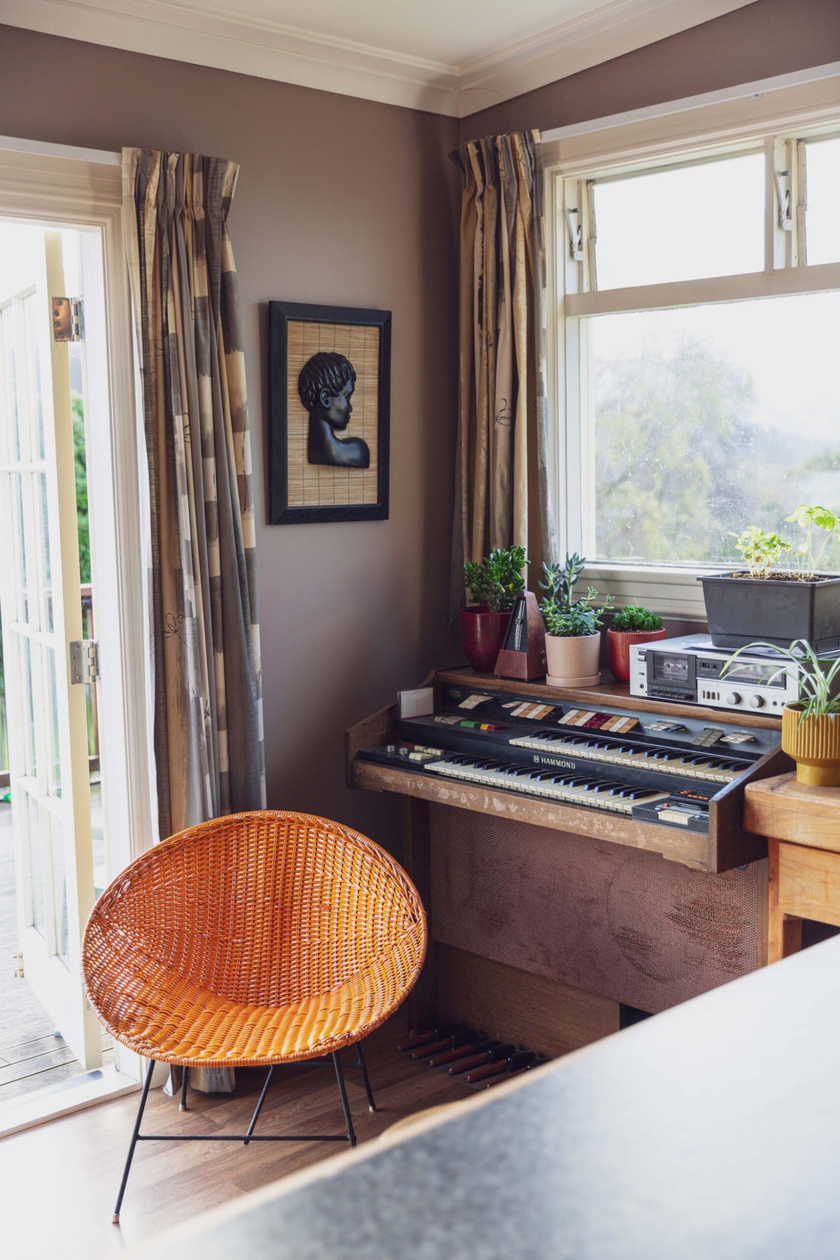Brown round rattan chair next to a vintage electric organ on a brown table 