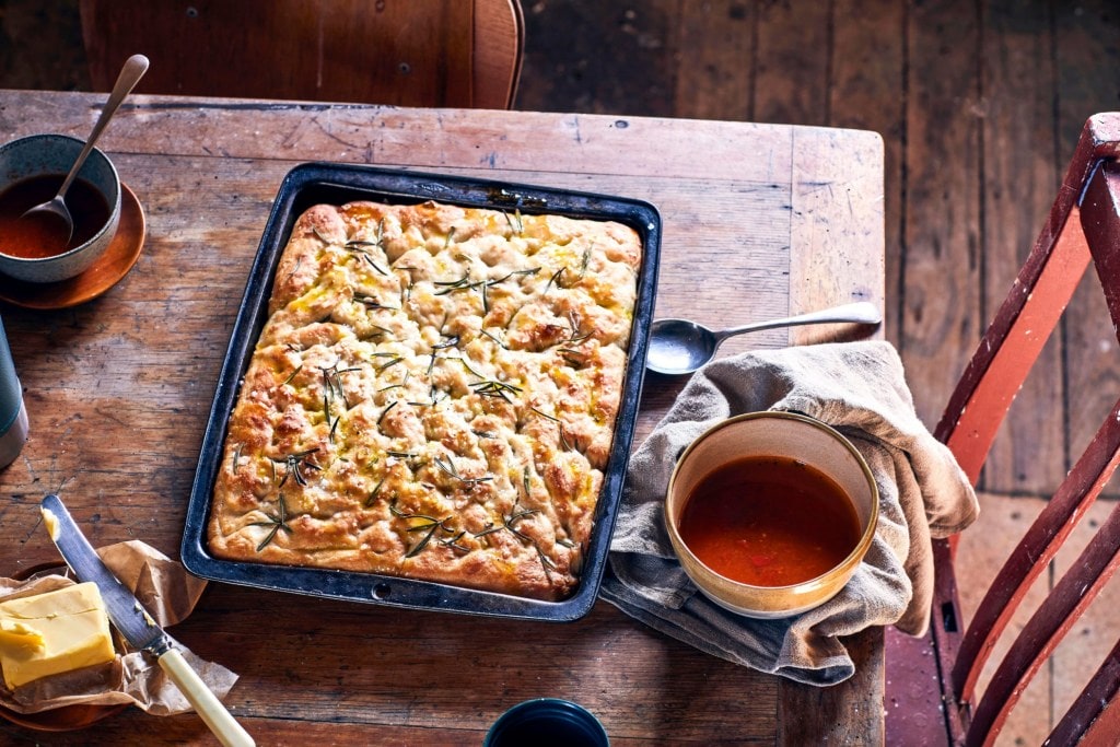 A black tray with rosemary and sea salt focaccia set on a brown table