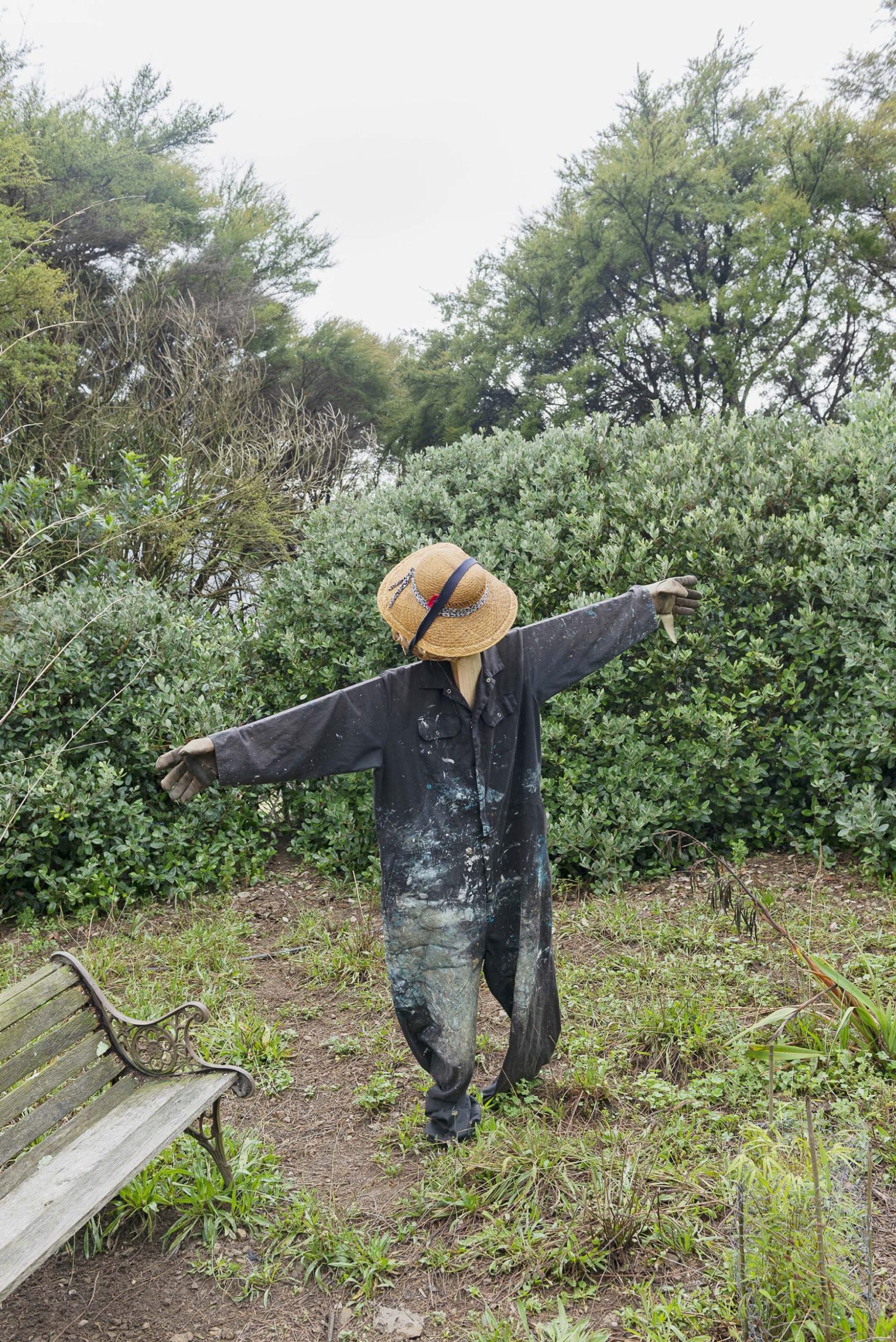 A scarecrow made out of a black paint splattered jumpsuit and a straw hat