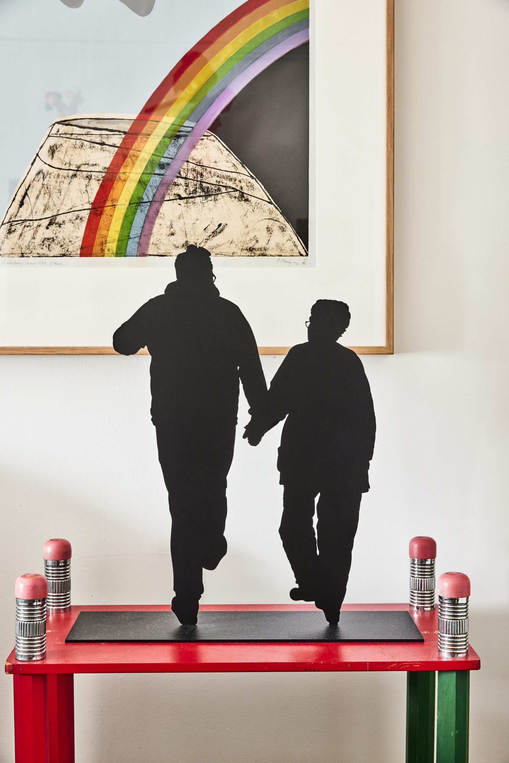 A black sculpture by artist Wayne Youle depicting David Alsop walking while holding hands with his mother on a red table