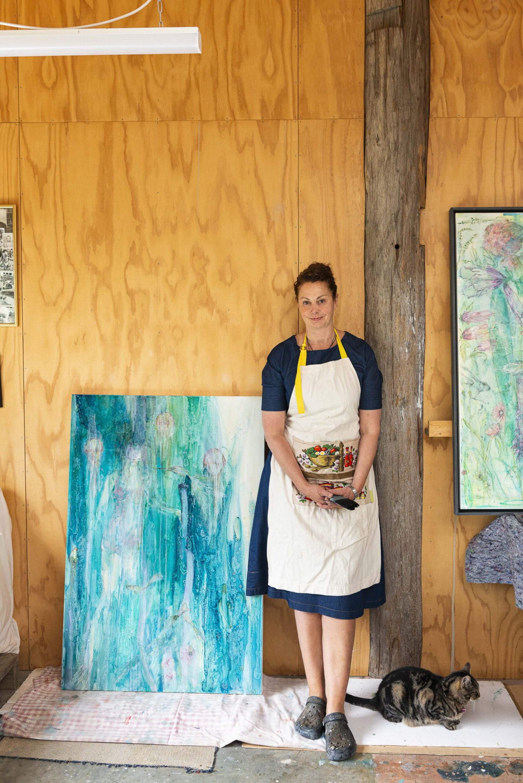 Serena Buonaguidi-Haynes standing by a large blue canvas with her cat Possum