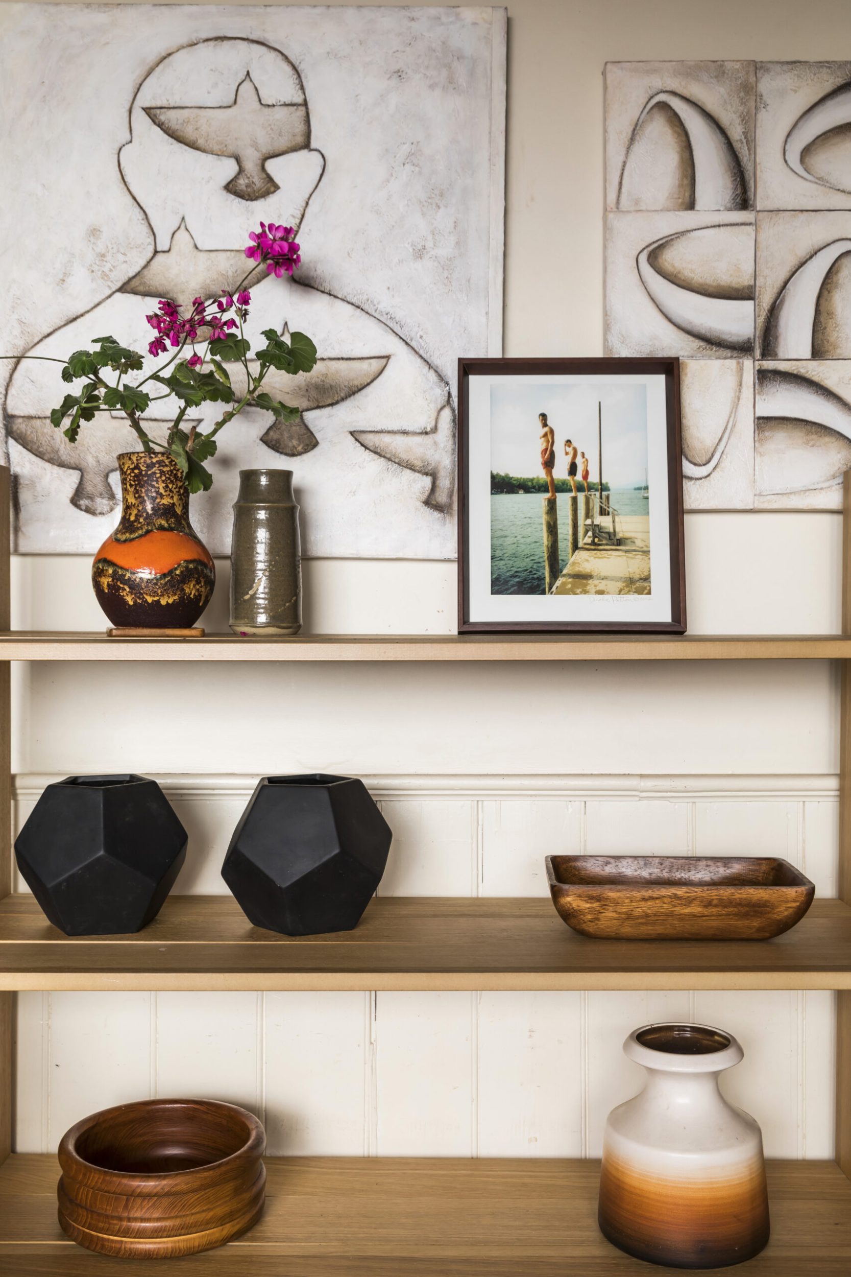 Wooden shelves with assorted black bases, a framed picture and a vase of pink flowers