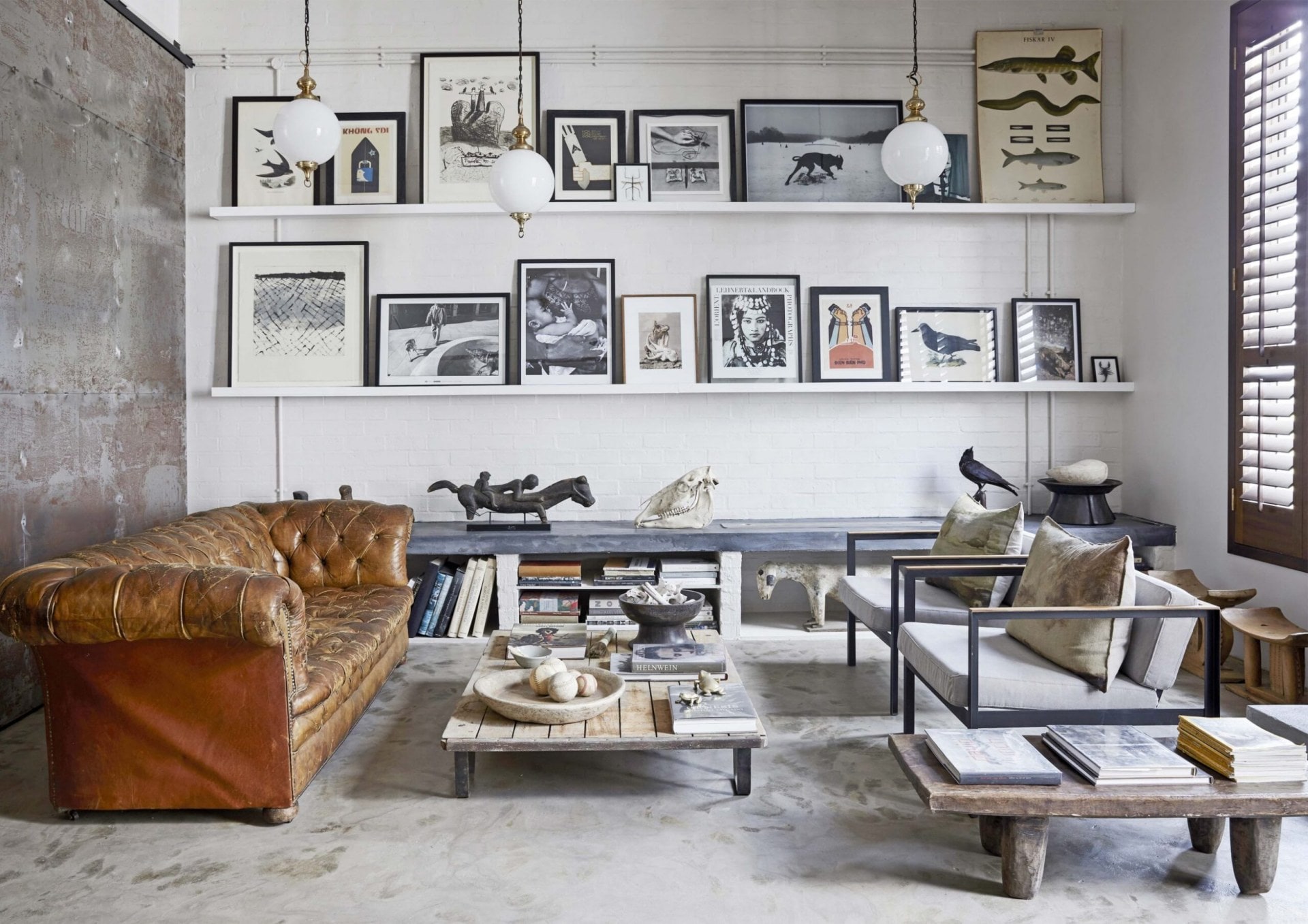 Living room with cement floors, concrete and white walls, two long shelves with assorted framed art