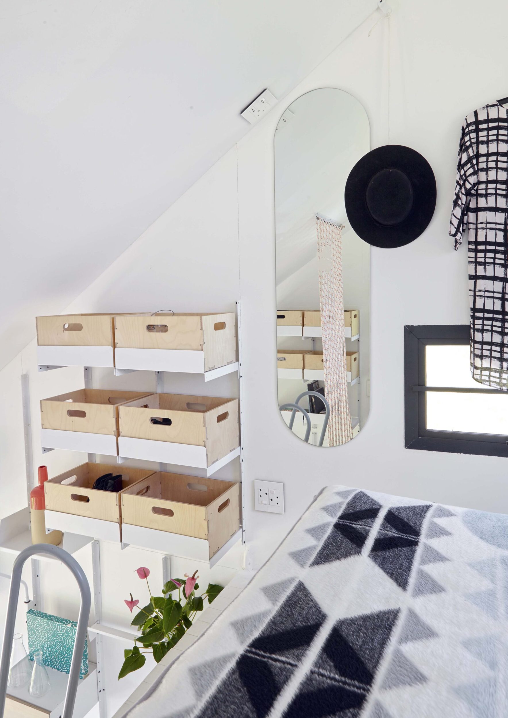 Small bedroom with wooden shelves, oval hanging mirror and patterned black and white bedspread
