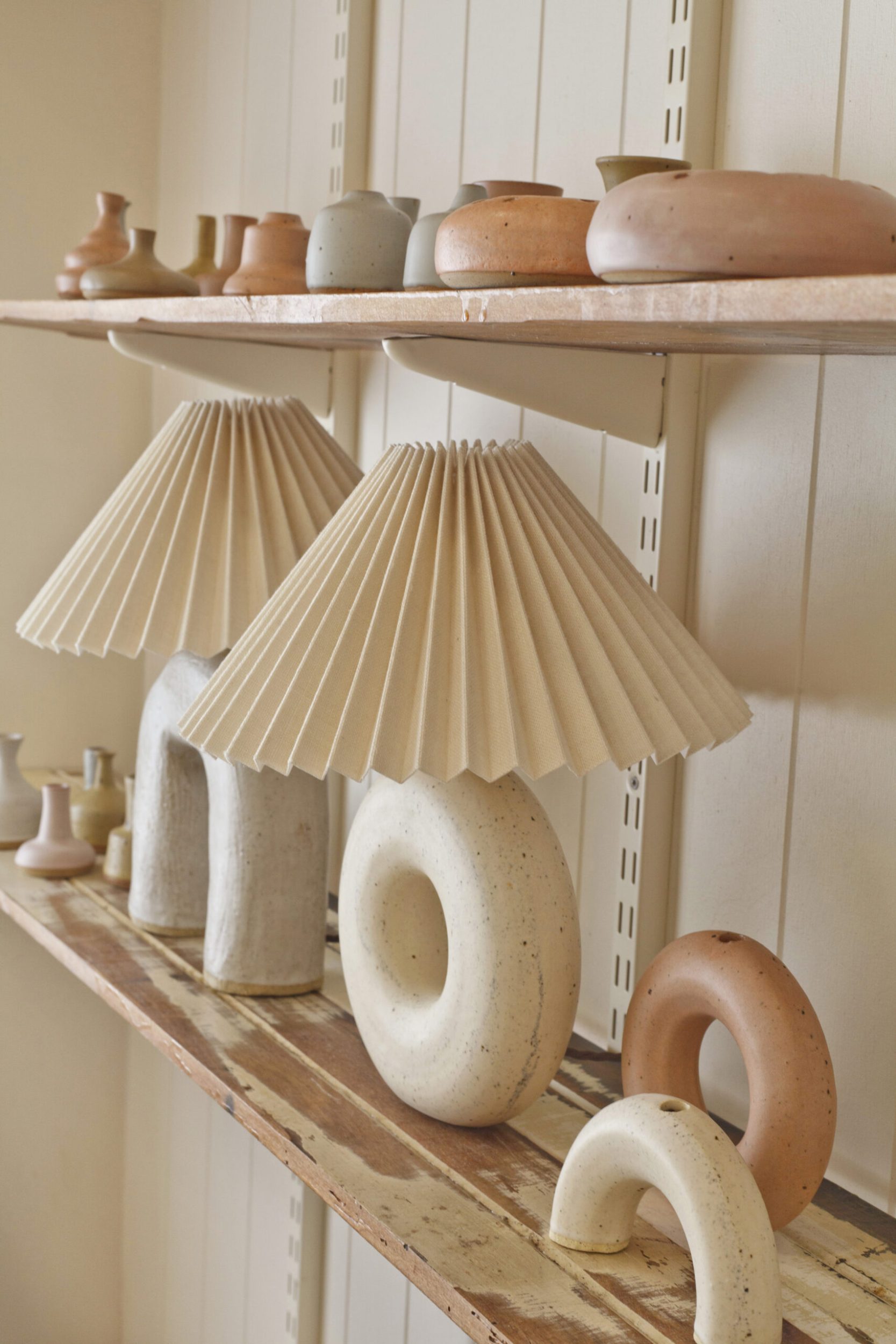 Brown woodwashed shelves holding Deborah Sweeney's ceramics and lamps. Their colours are white, grey and terracotta orange