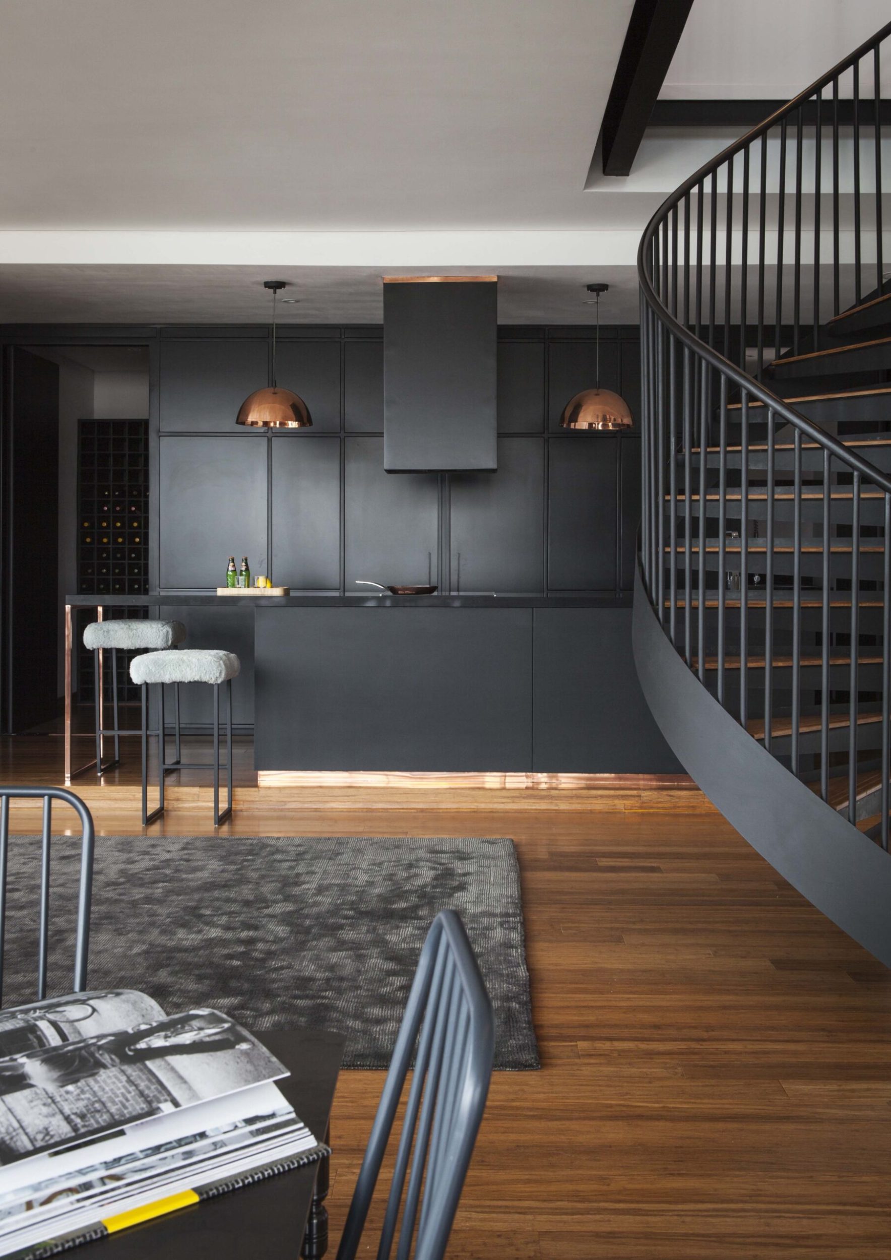 A kitchen with wood floors and brass hanging lamps and black walls and shelves