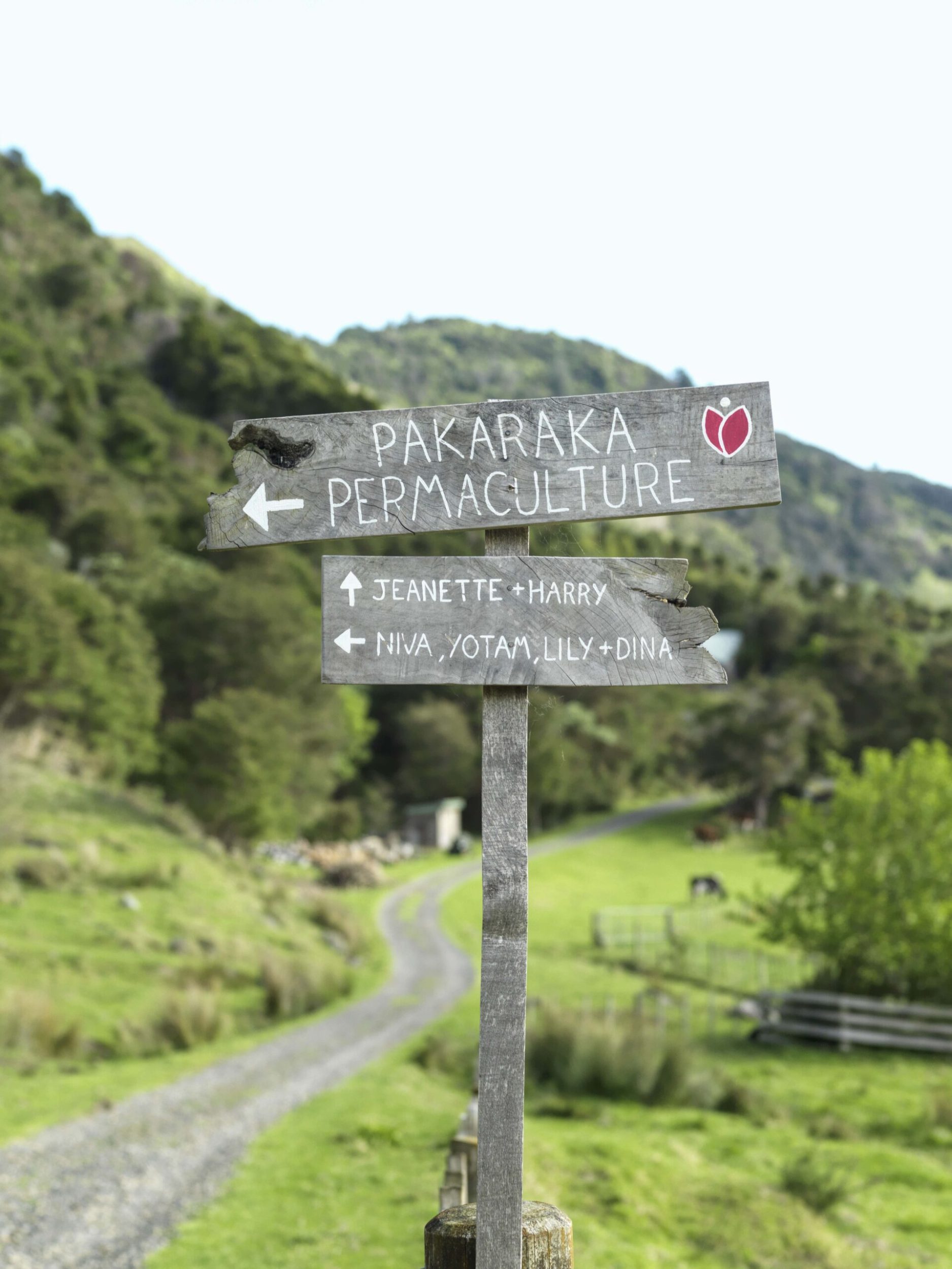 Wood sign with an arrow pointing left saying Pakaraka Permaculture and Niva, Yotam, Lily and Dina, and pointing forward saying Jeannette and Harry