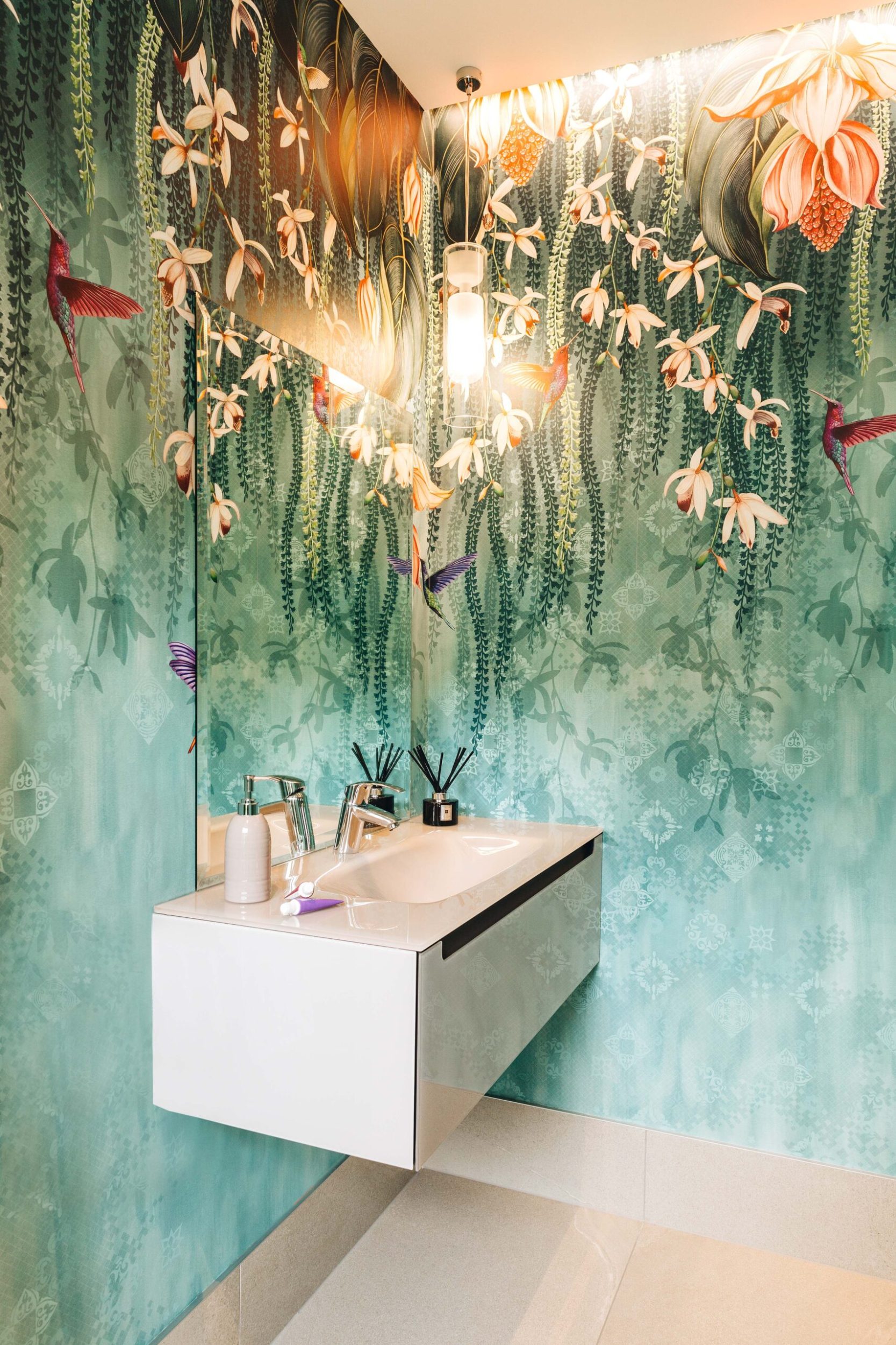 A bathroom with a green and floral patterned Osborne & Little  ‘Trailing Orchid’ wallpaper