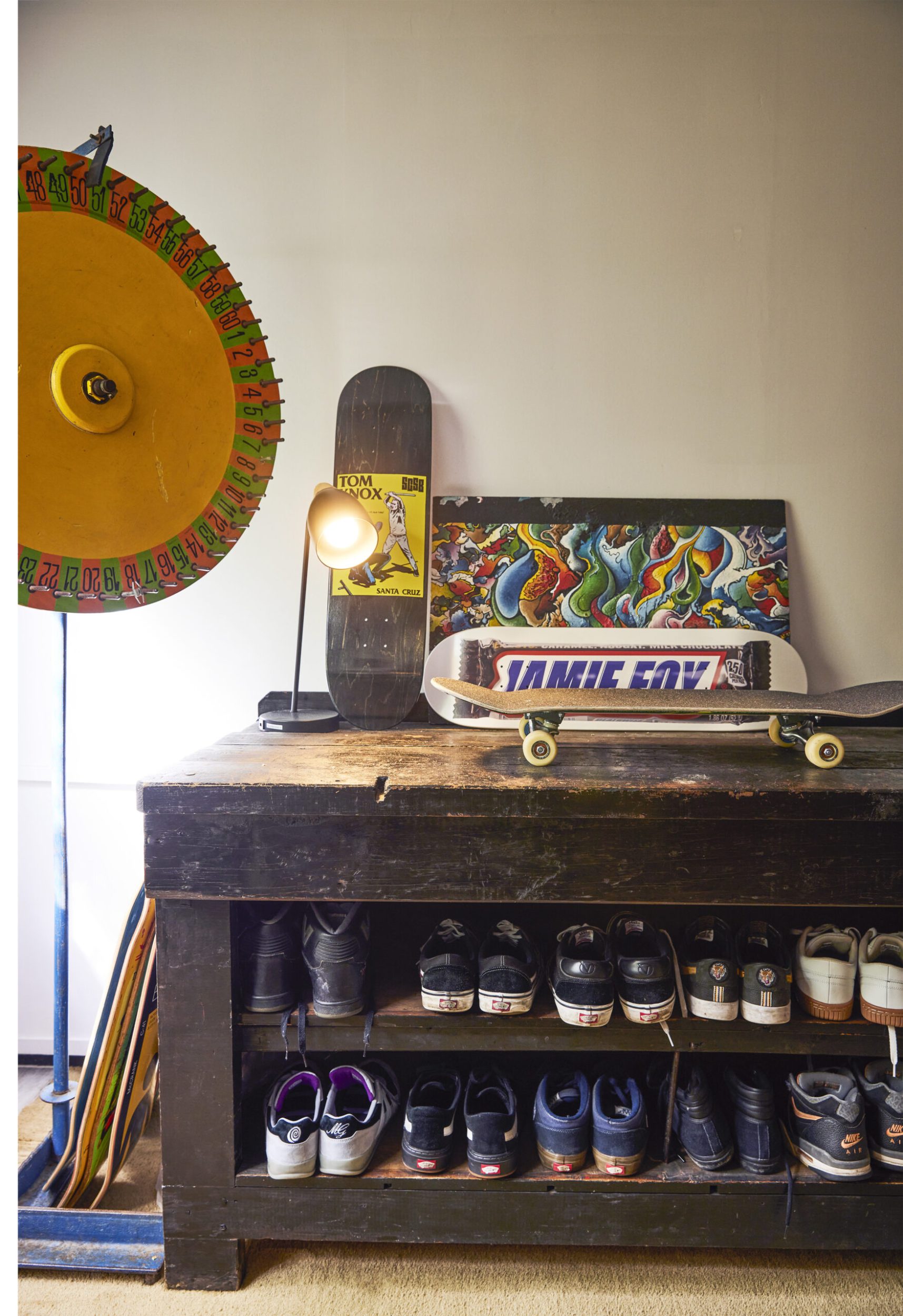 Black vintage cabinet with shoes on shelves and assorted art and a skateboard on top