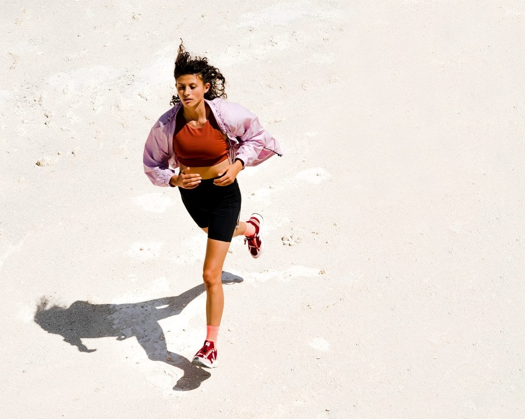 Woman running on white sand while wearing pink and red outfit