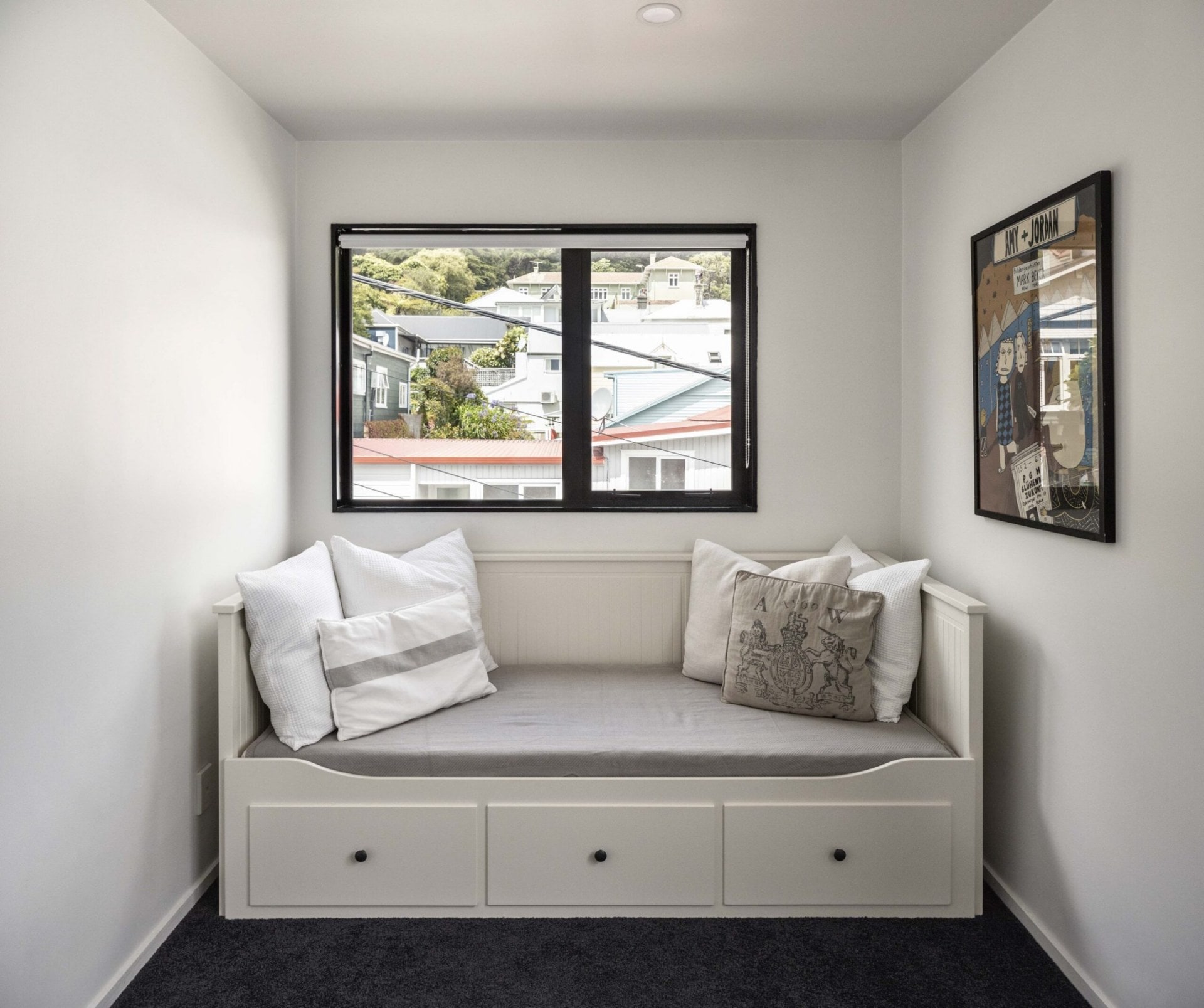 A white room with a white fold out couch bed and a window with a black windowframe