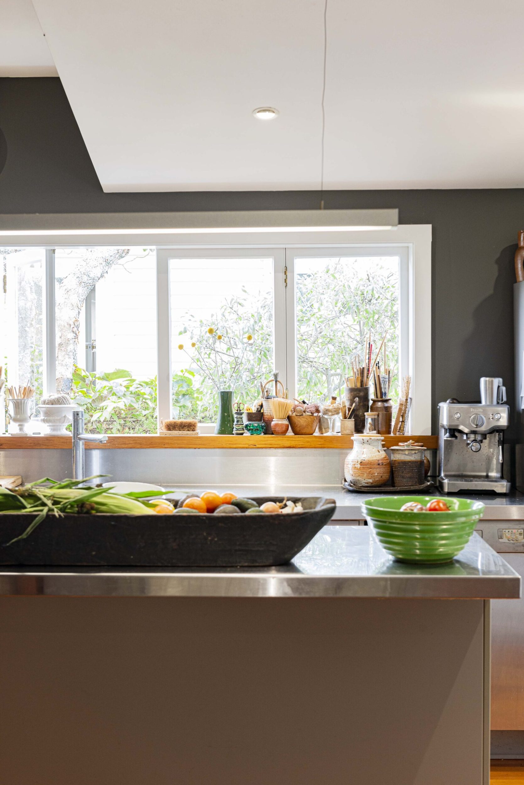 A black kitchen with a stainless steel benchtop with bowls of fruit and vegetables