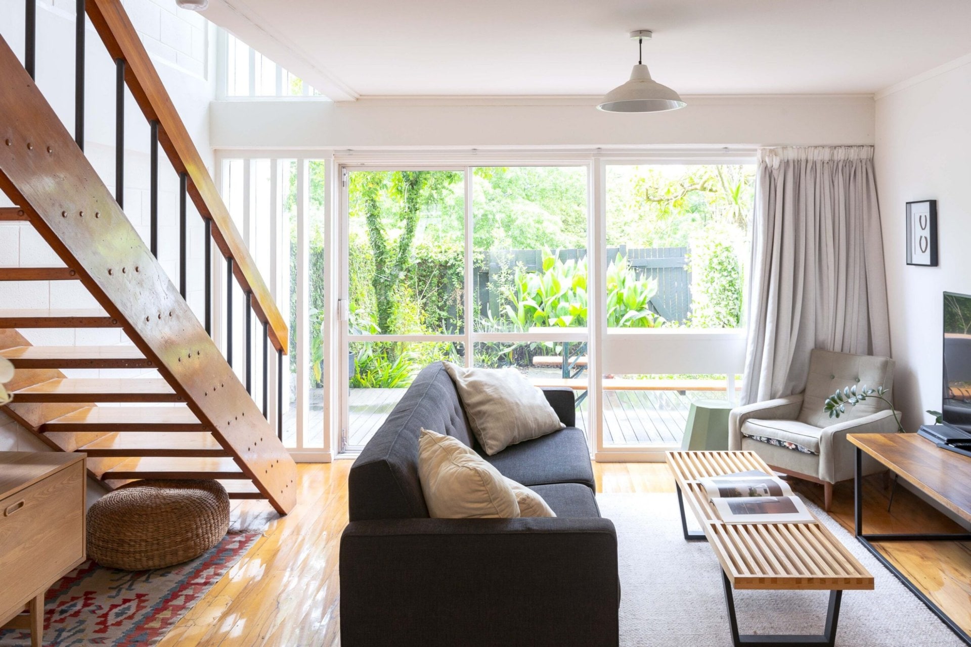 Living room with wooden floors, angled stairs, a black couch and sliding deck doors 