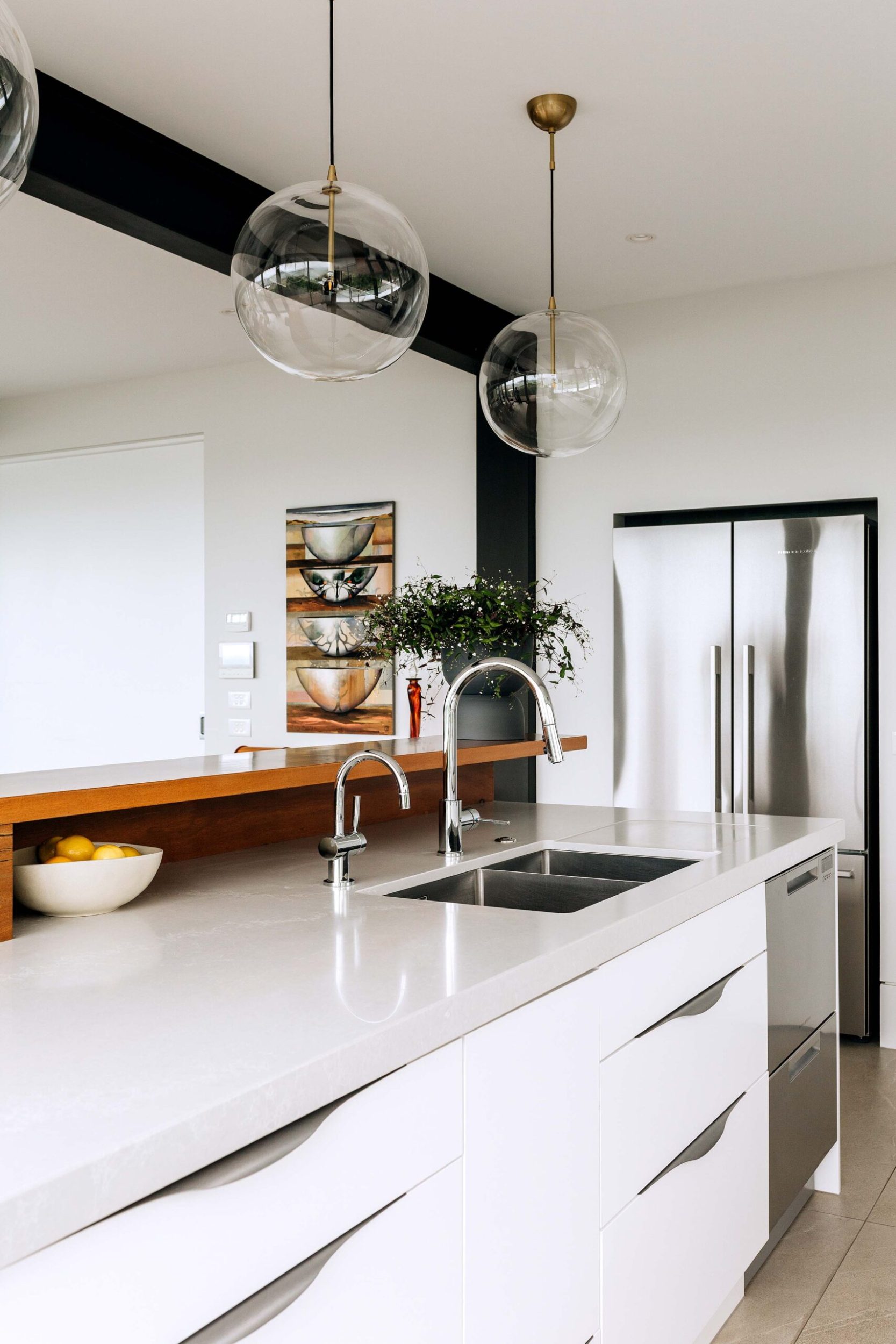 Kitchen with silver finishings, a white marble benchtop and hanging glass pendant lights