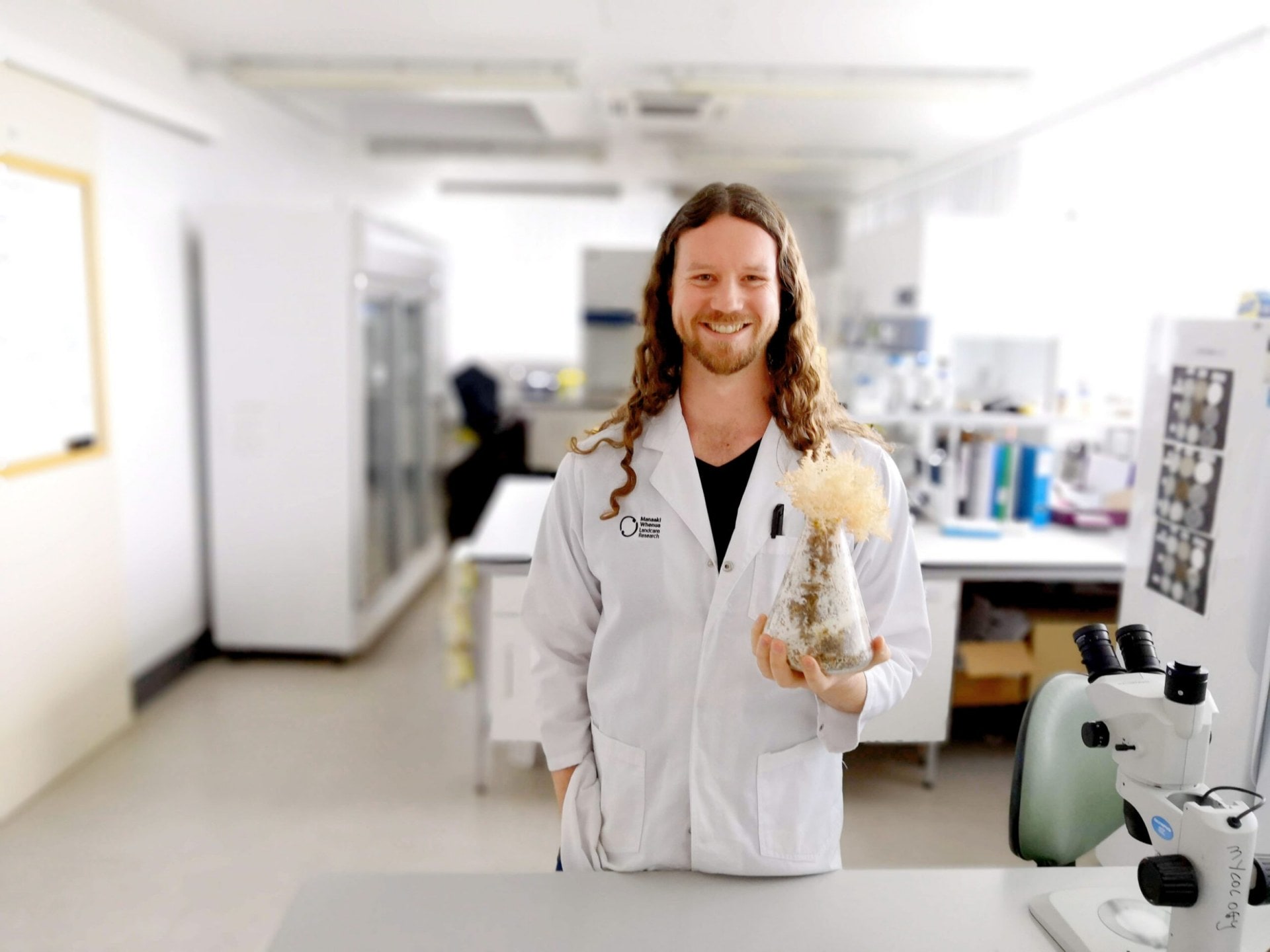 Chris Smith in white lab coat holding a fungi specimen 