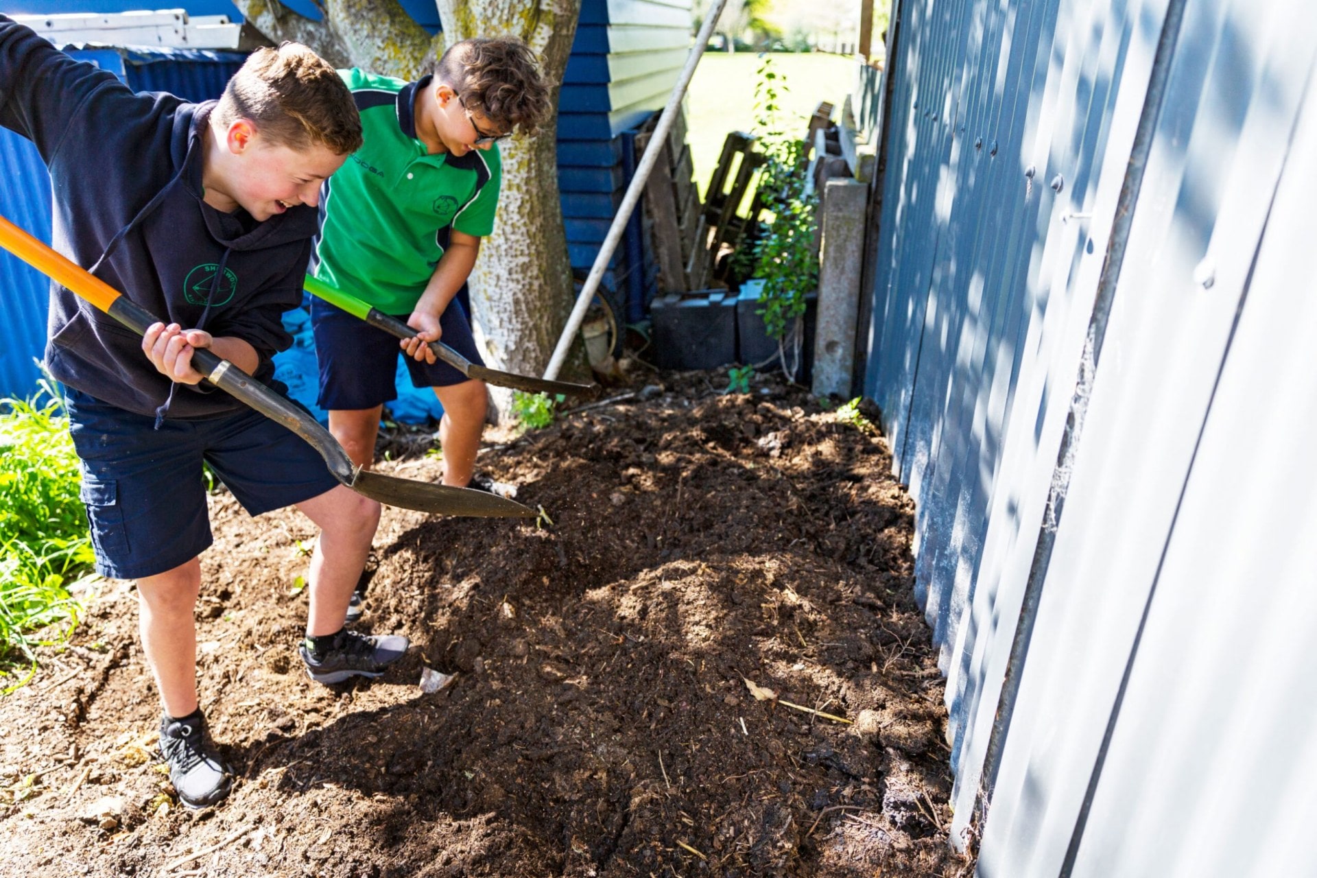 Two boys digging with spades in compost