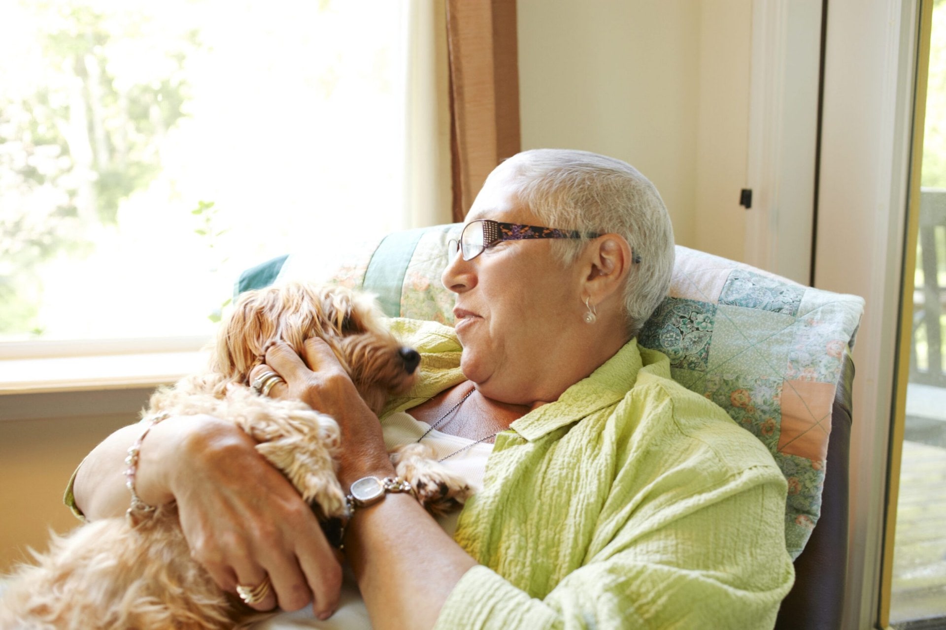 Elderly lady sitting in an armchair holding a tan dog