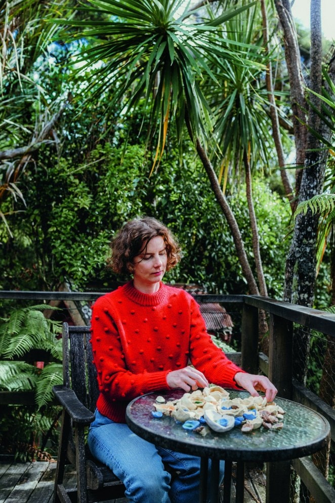 Kate Newby sitting on a deck by a round table laden with white shells 