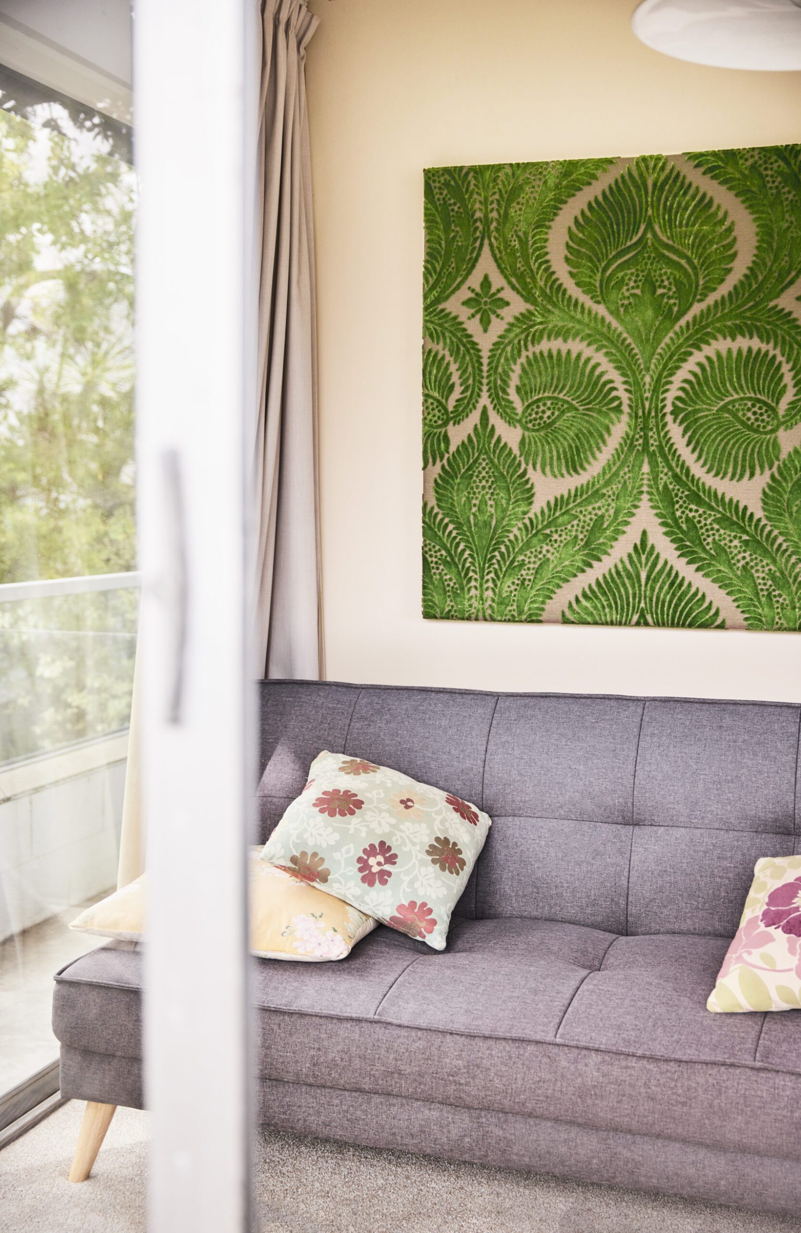 A green and white canvas artwork made of makum fabric hanging above grey couch