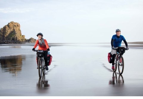a man and a woman riding bikes on the beach with 2 metres between them
