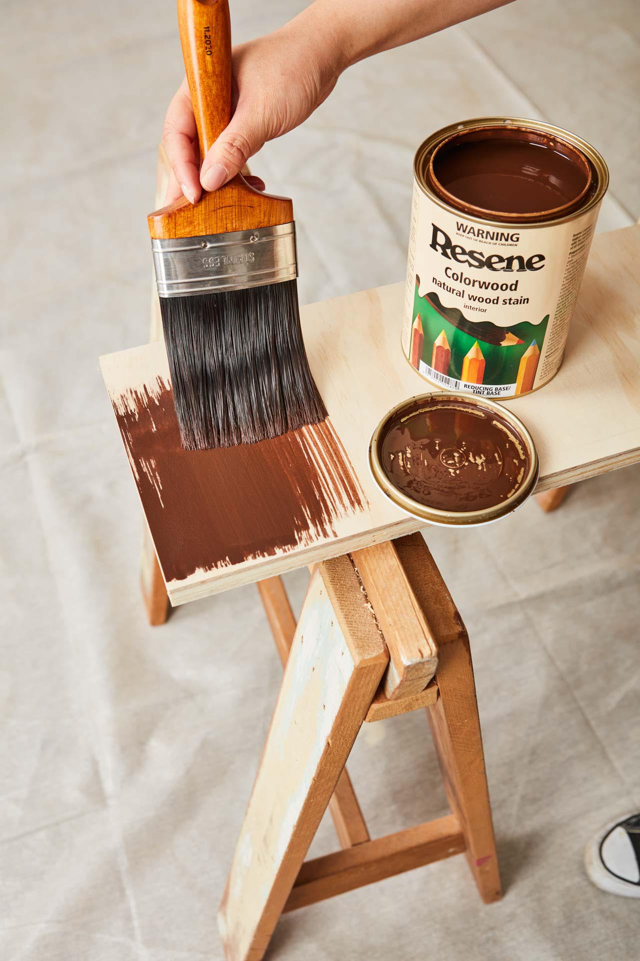 Plank of plywood being stained with dark brown wood stain