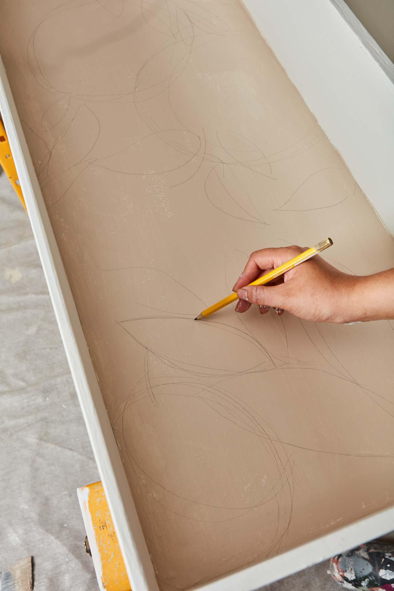 Hand sketching leaf shapes onto the inside of a drawer with a pencil