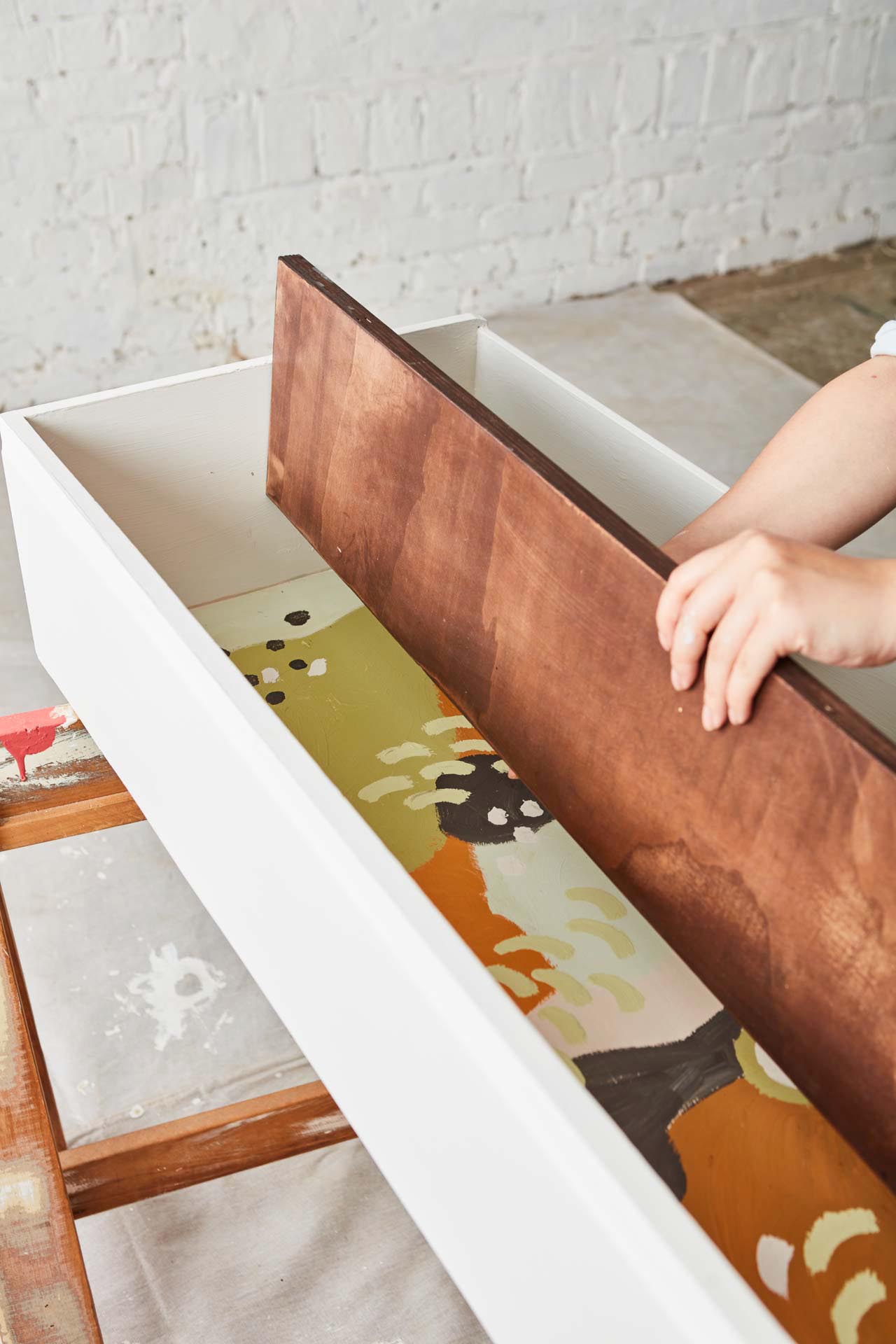 Hands placing a dark stained piece of wood inside a painted drawer