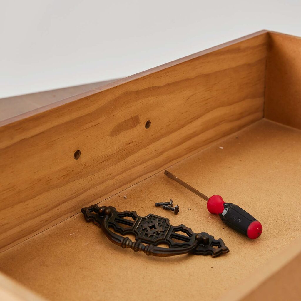 A screwdriver next to screws and the drawers hardware