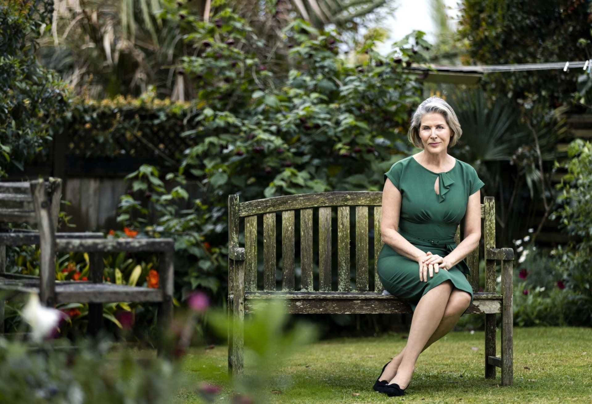 Jennifer Ward-Lealand sitting in a green dress on a garden bench