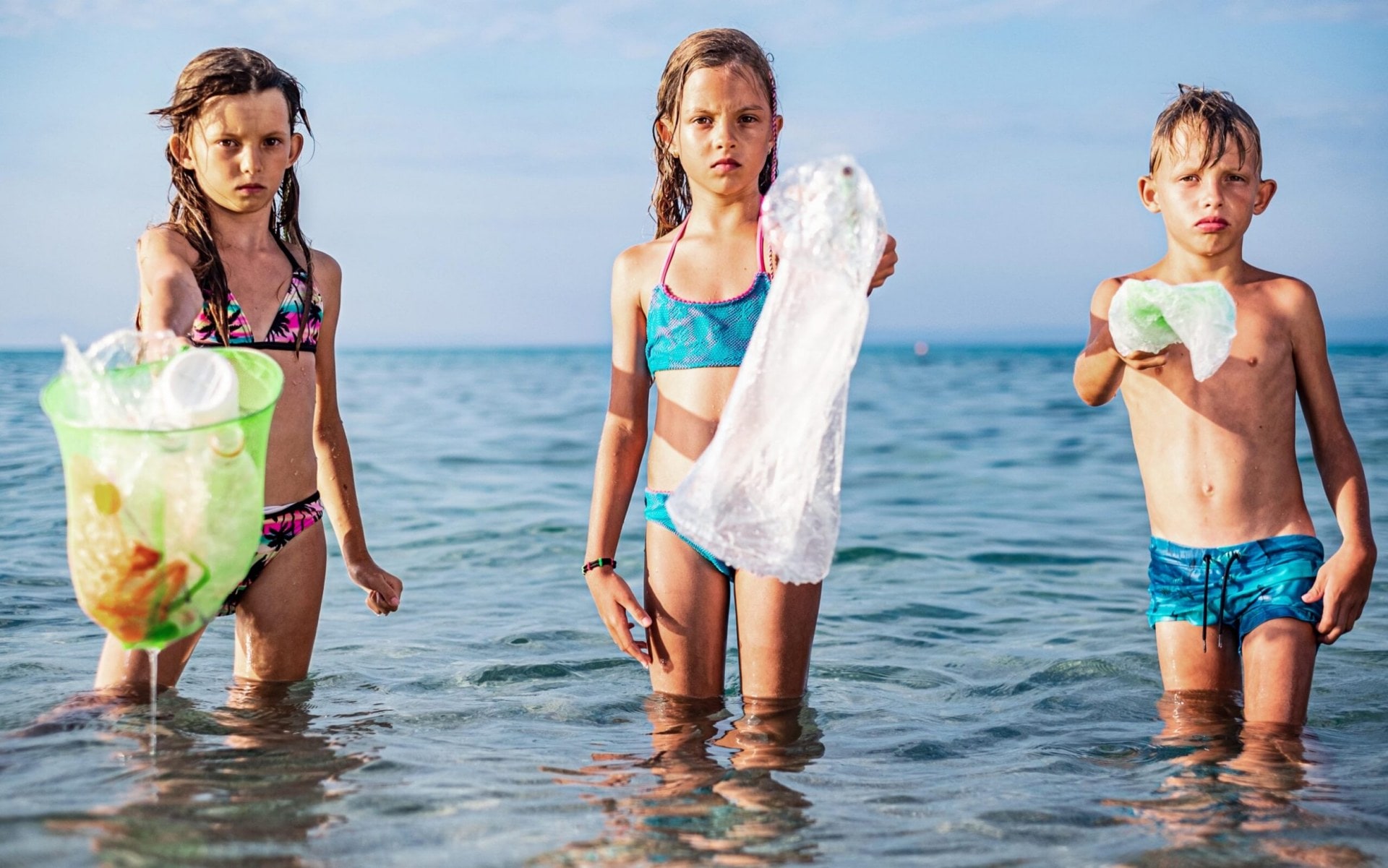 three children holding plastic waste in the ocean