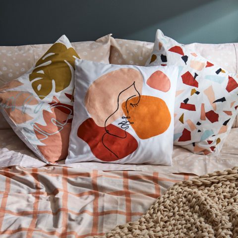 Pillows with abstract designs on a bed with a peach duvet